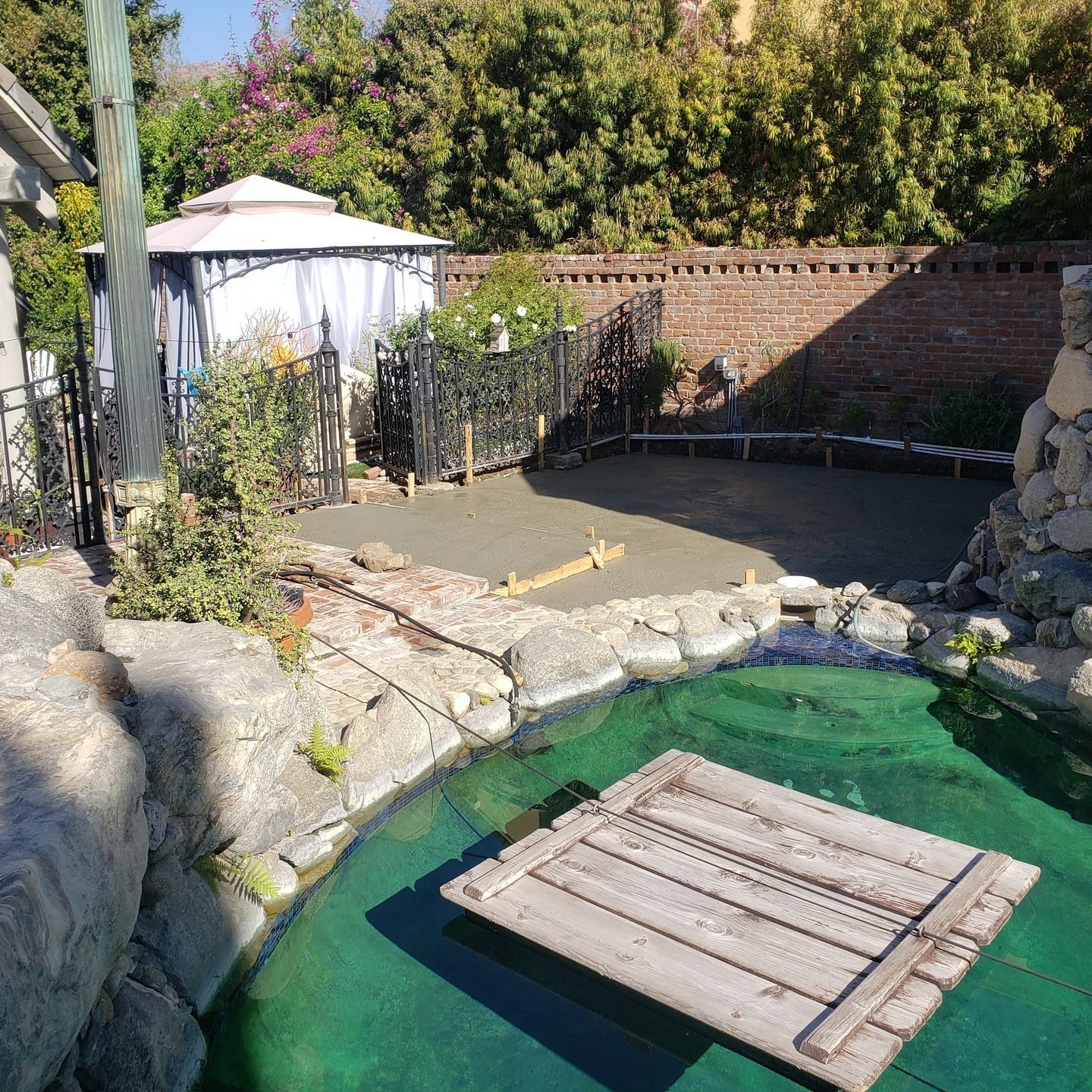 Backyard with a gazebo, small pond, new concrete, and brick wall.