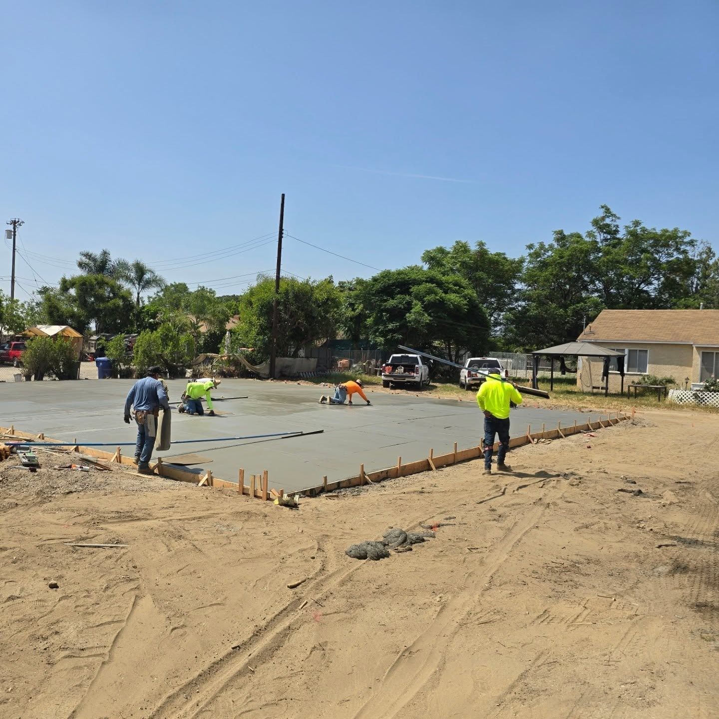 Construction workers pouring and smoothing concrete for a new foundation on a sunny day.