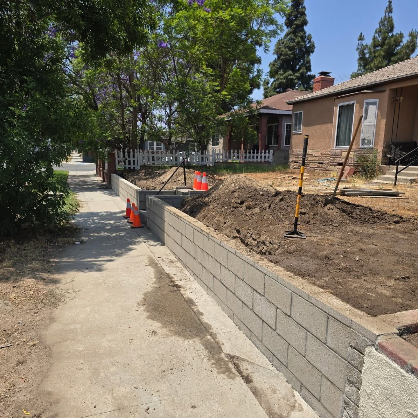 Sidewalk with a new cinder block retaining wall under construction in front of houses.