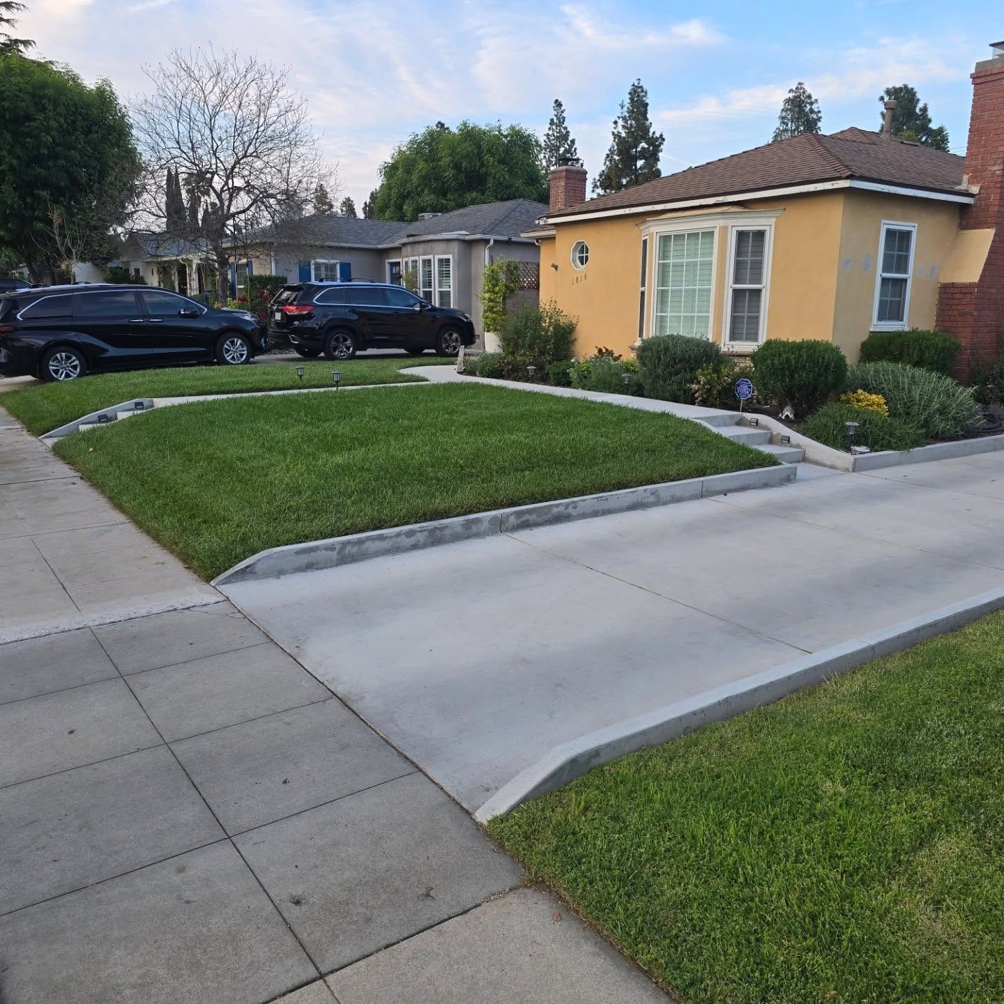 Houses with well-kept lawns and driveways. Cars are parked on the street.