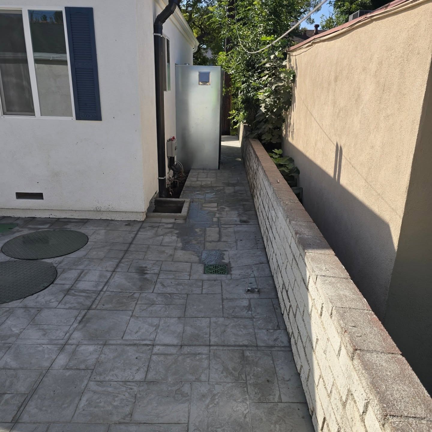 Narrow concrete pathway between a white building and tan wall.