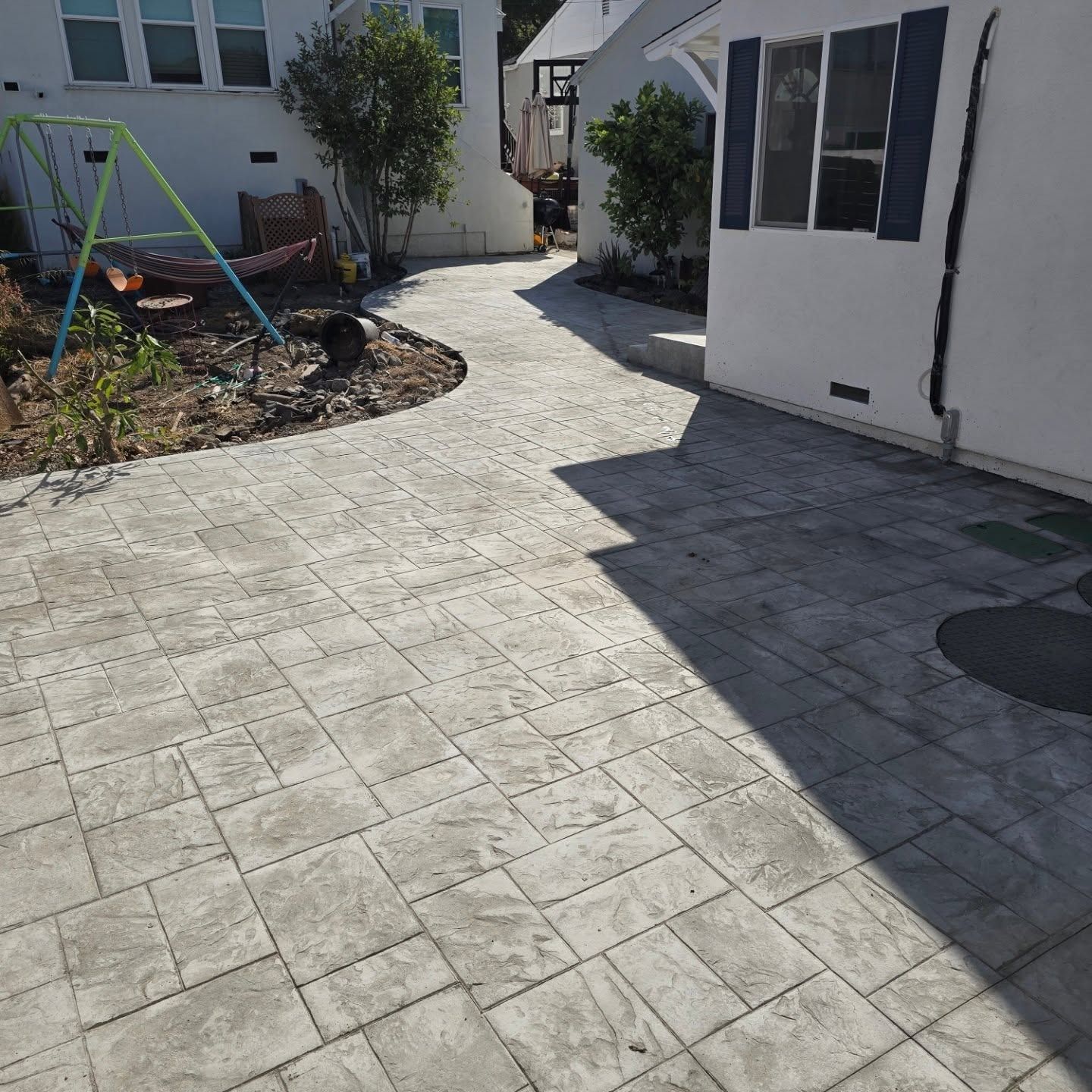 Stamped concrete patio and walkway beside a white house with blue shutters, leading to a backyard.