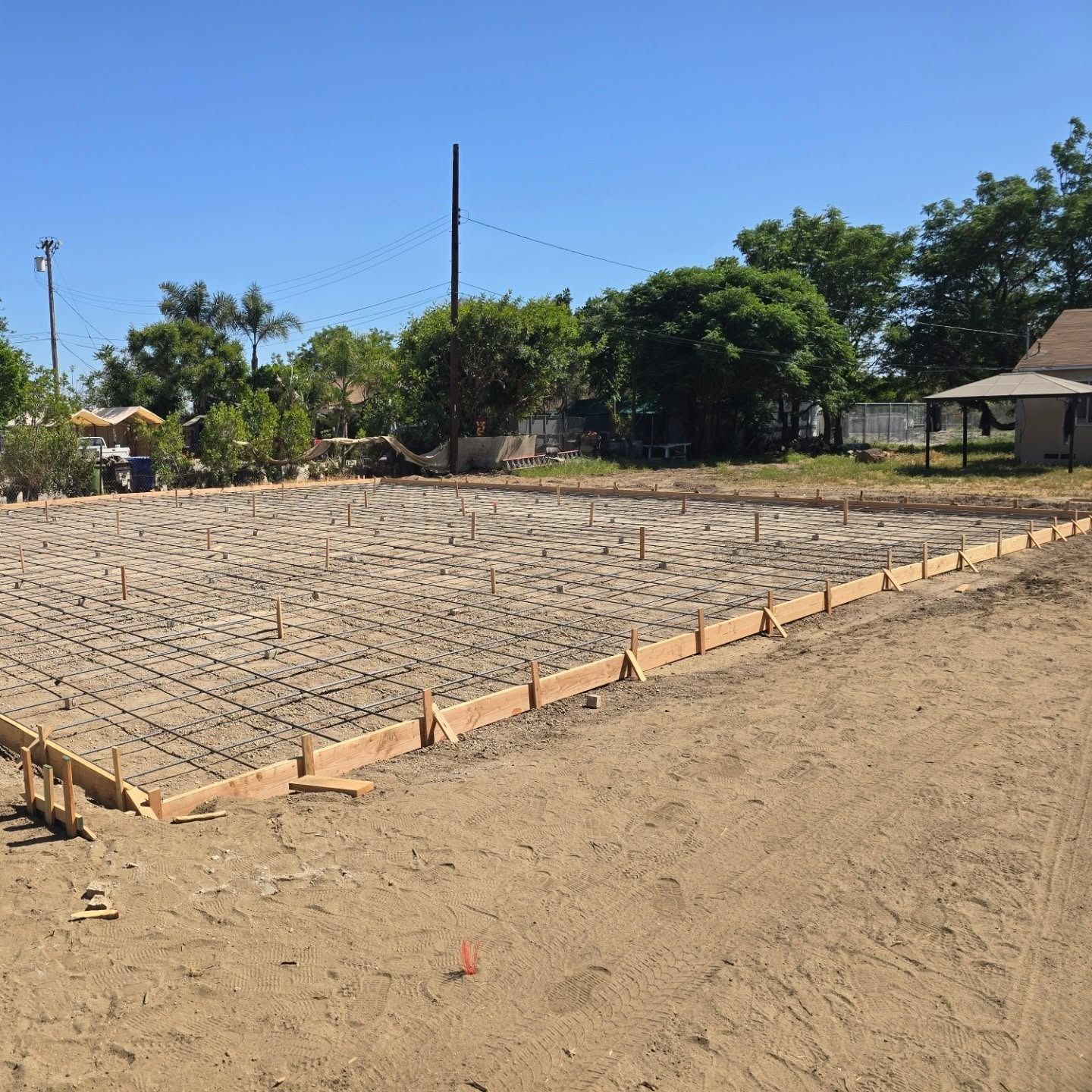 Wooden forms and rebar grid on a graded dirt site, ready for concrete, sunny day.