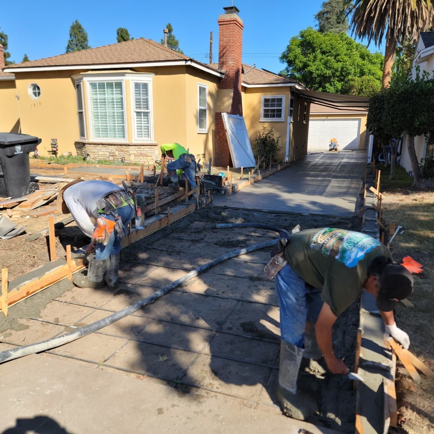 Construction workers pouring concrete for a driveway. Setting: a sunny residential area.