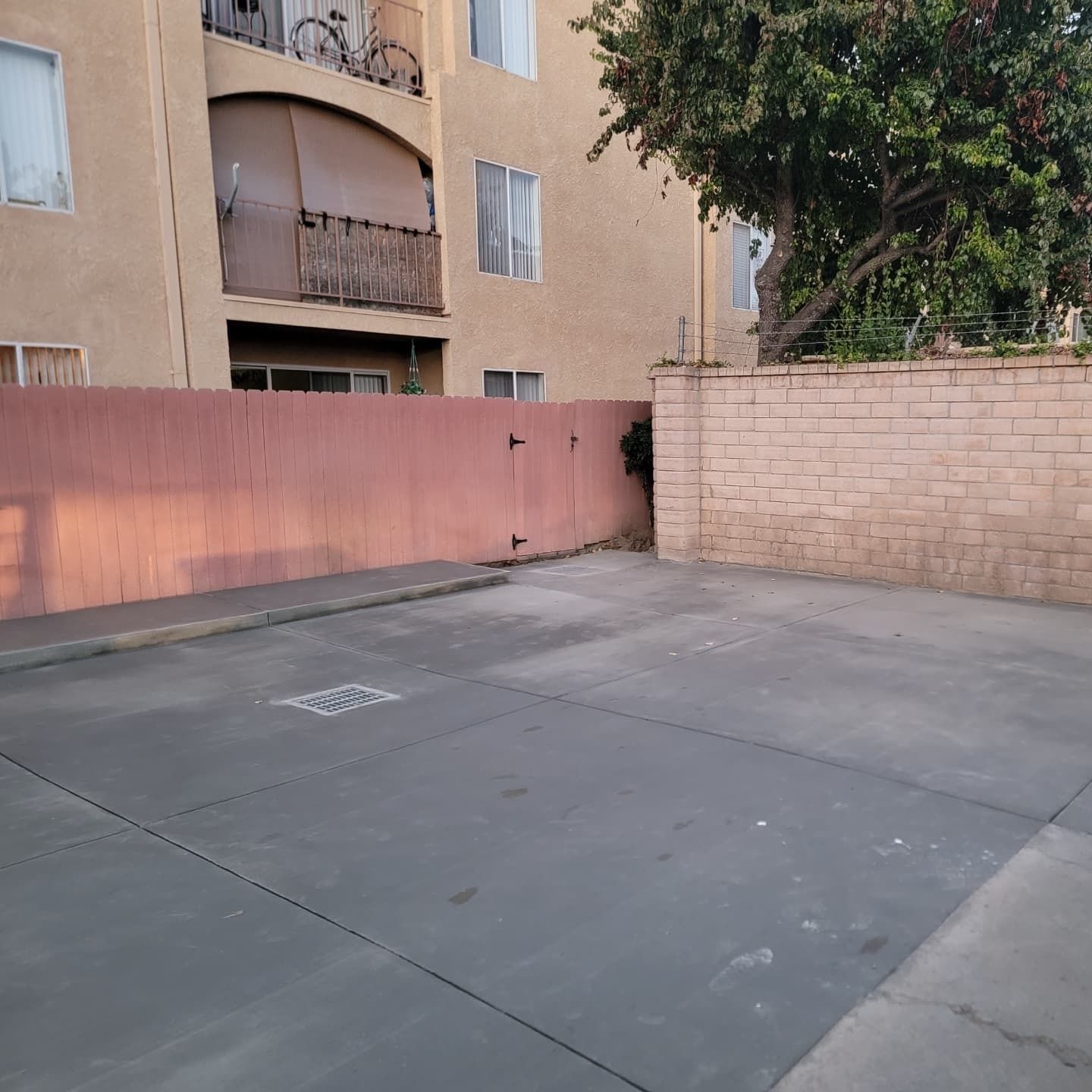 Empty concrete parking area next to a light brown building, with a red wall and brick wall.