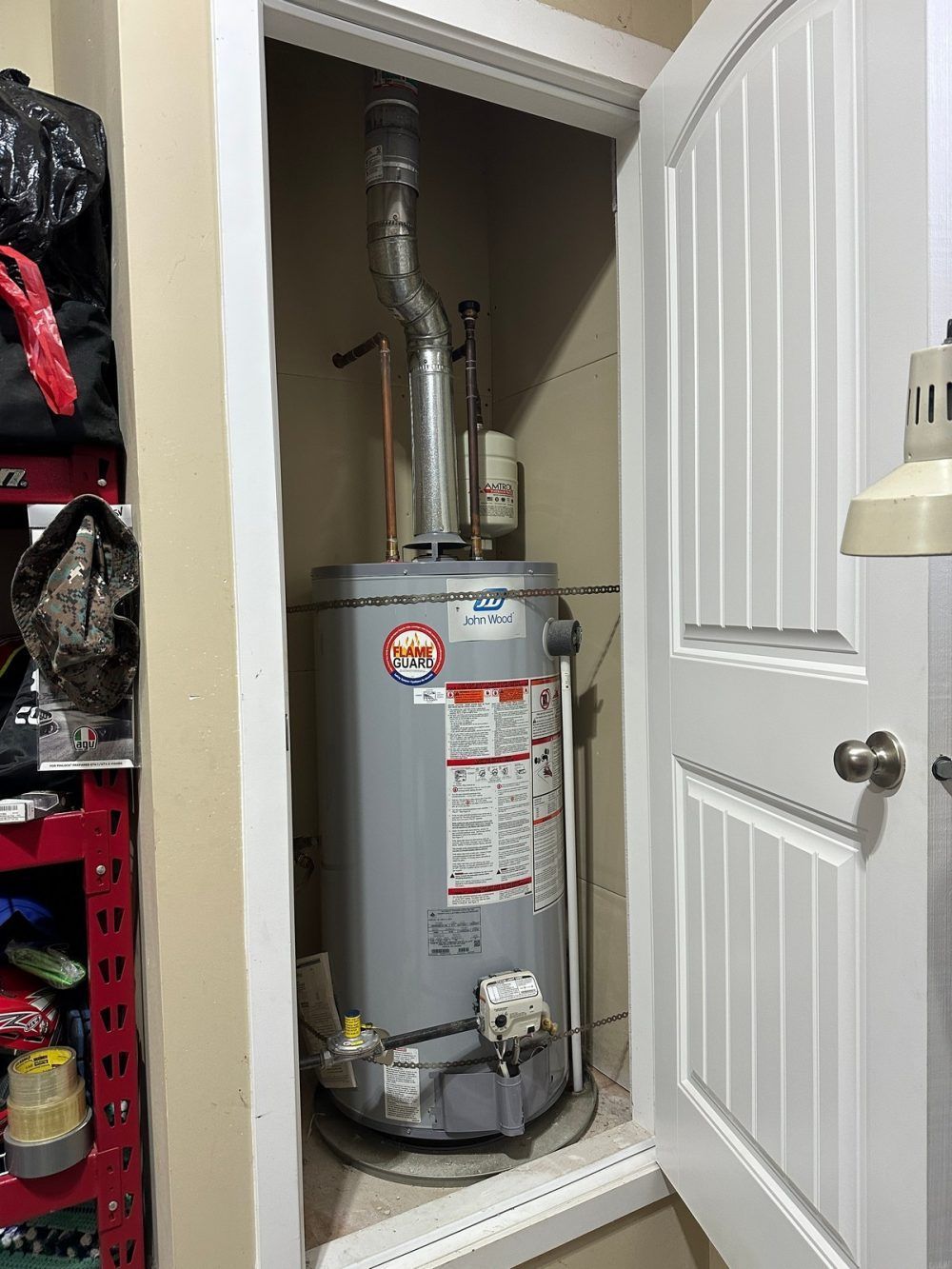 A water heater is sitting in a closet next to a door.