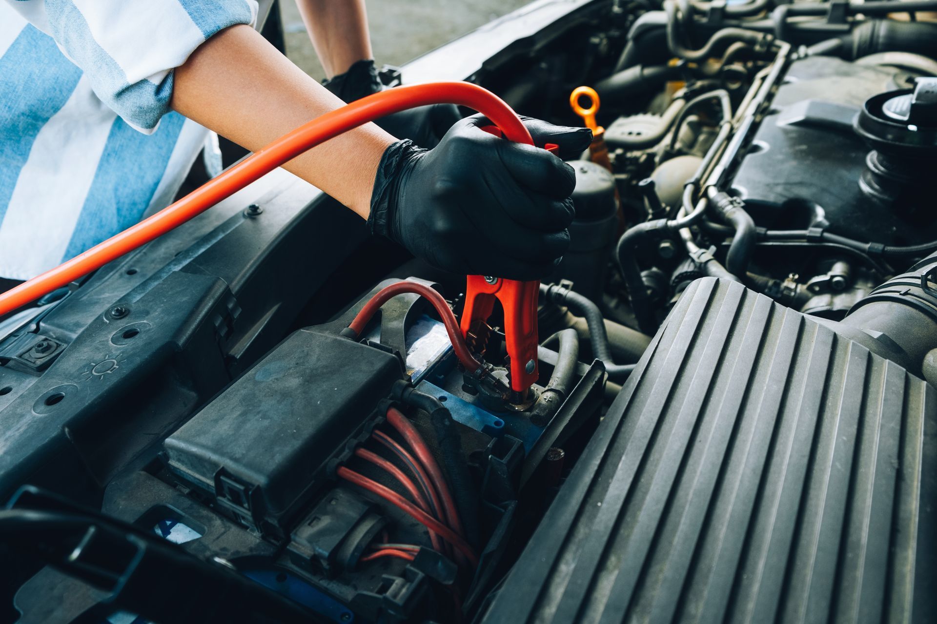 Person in black gloves connecting jumper cables to a car battery under the hood. Person in black gloves connecting jumper cables to a car battery under the hood.