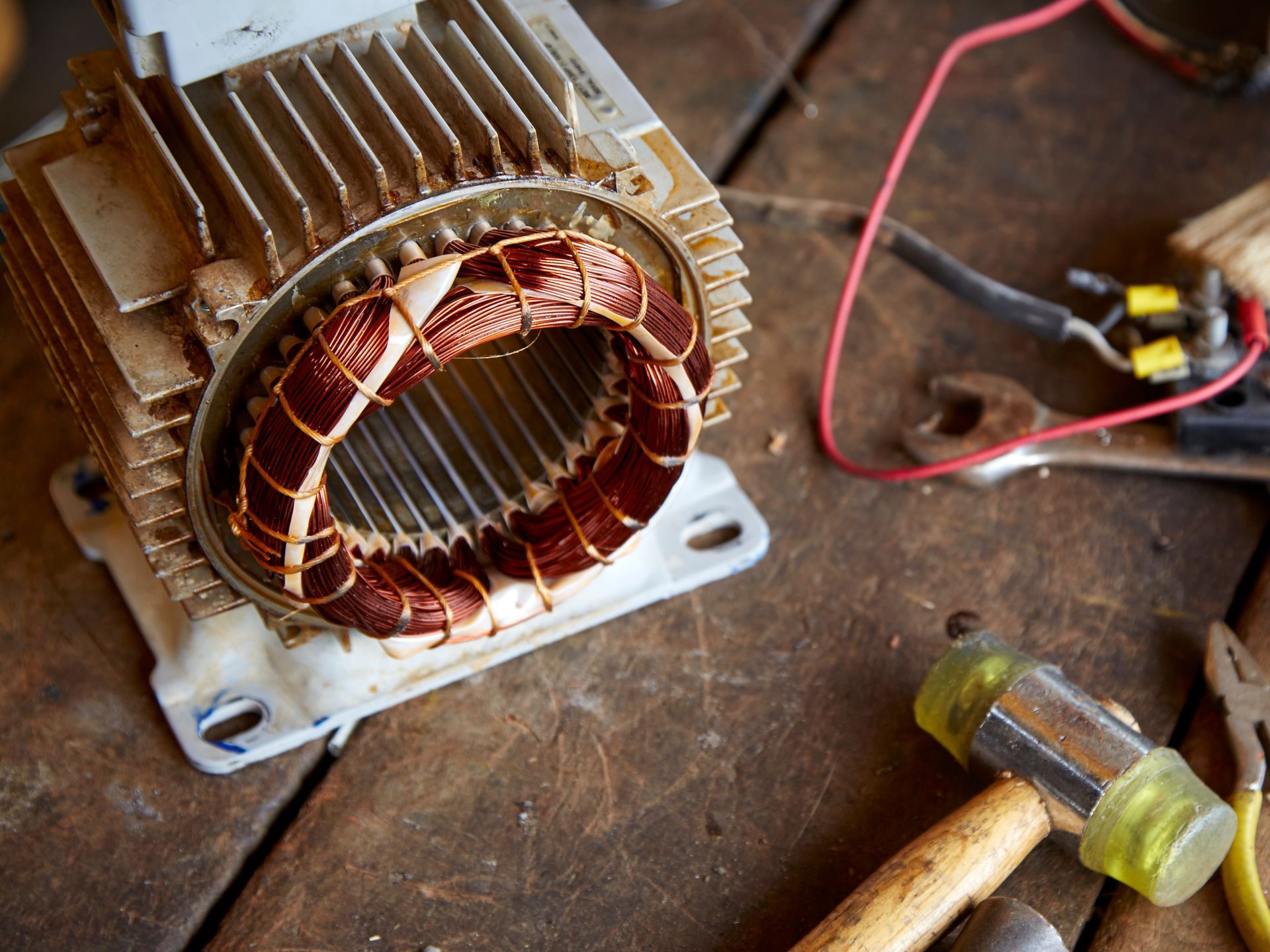 Electric motor with exposed copper windings on a wooden work surface, alongside tools. Electric motor with exposed copper windings on a wooden work surface, alongside tools.
