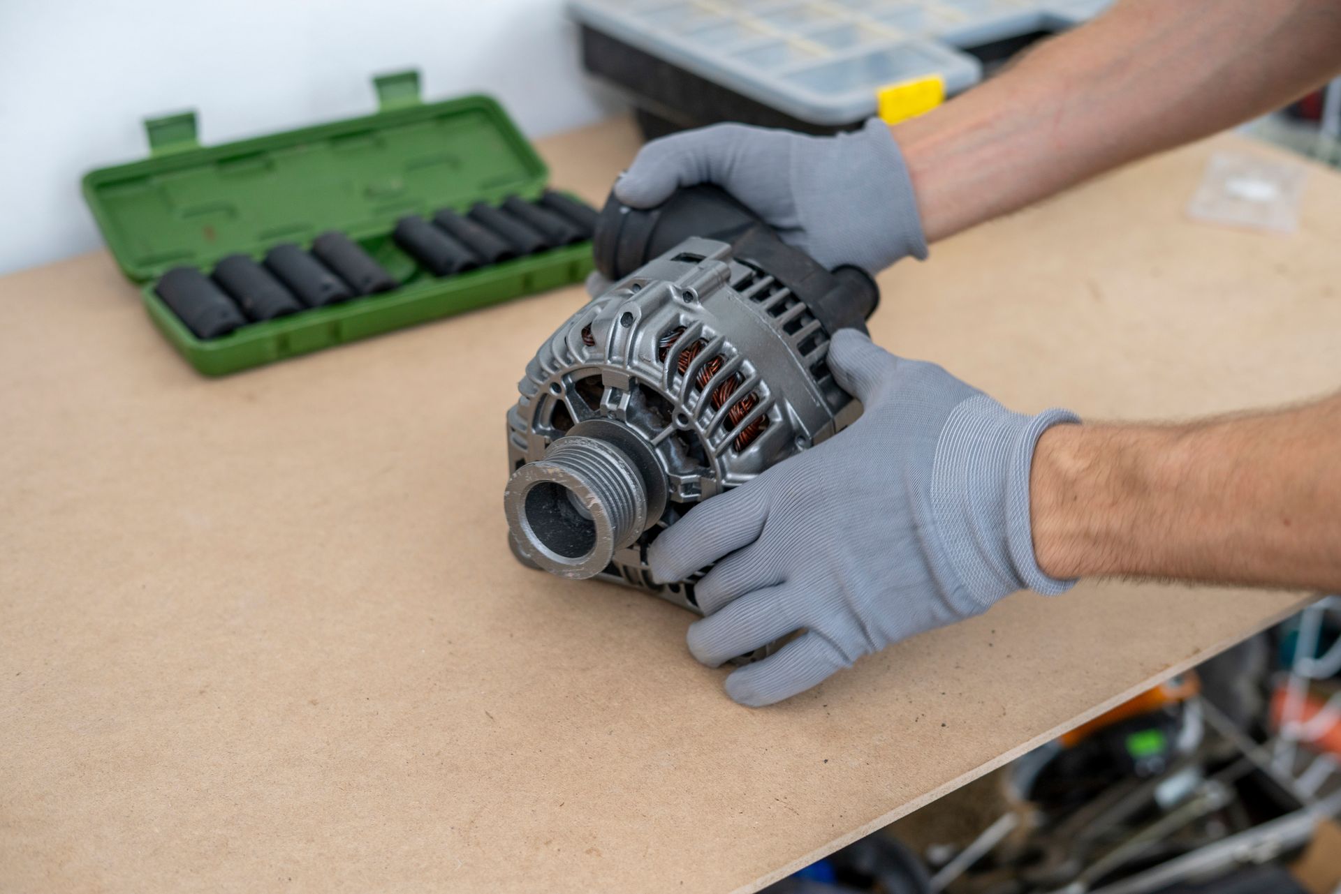 Hands in gray gloves holding a car alternator on a workbench with tools nearby. Hands in gray gloves holding a car alternator on a workbench with tools nearby.