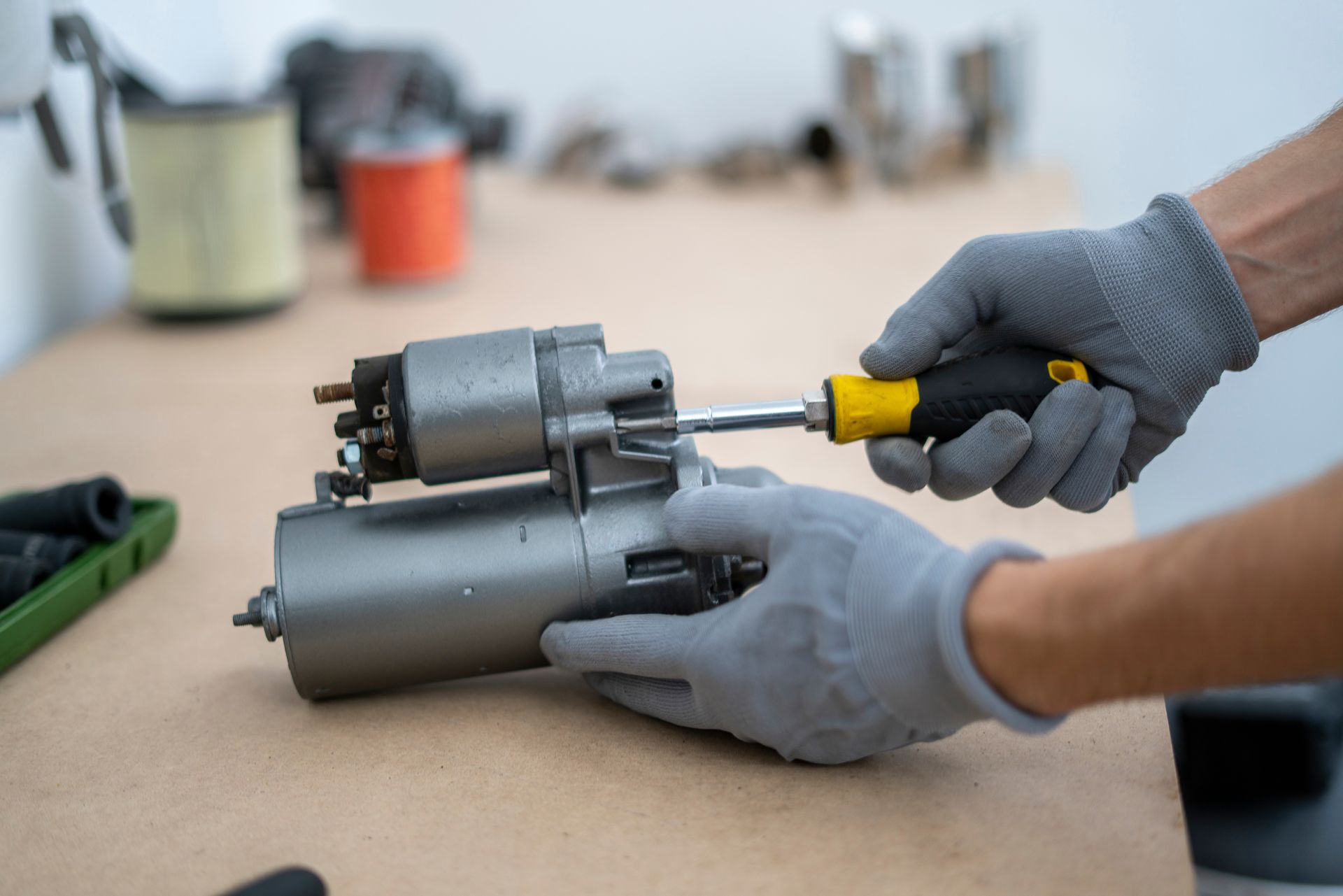 Hands in grey gloves using a screwdriver on a car starter motor in a workshop.