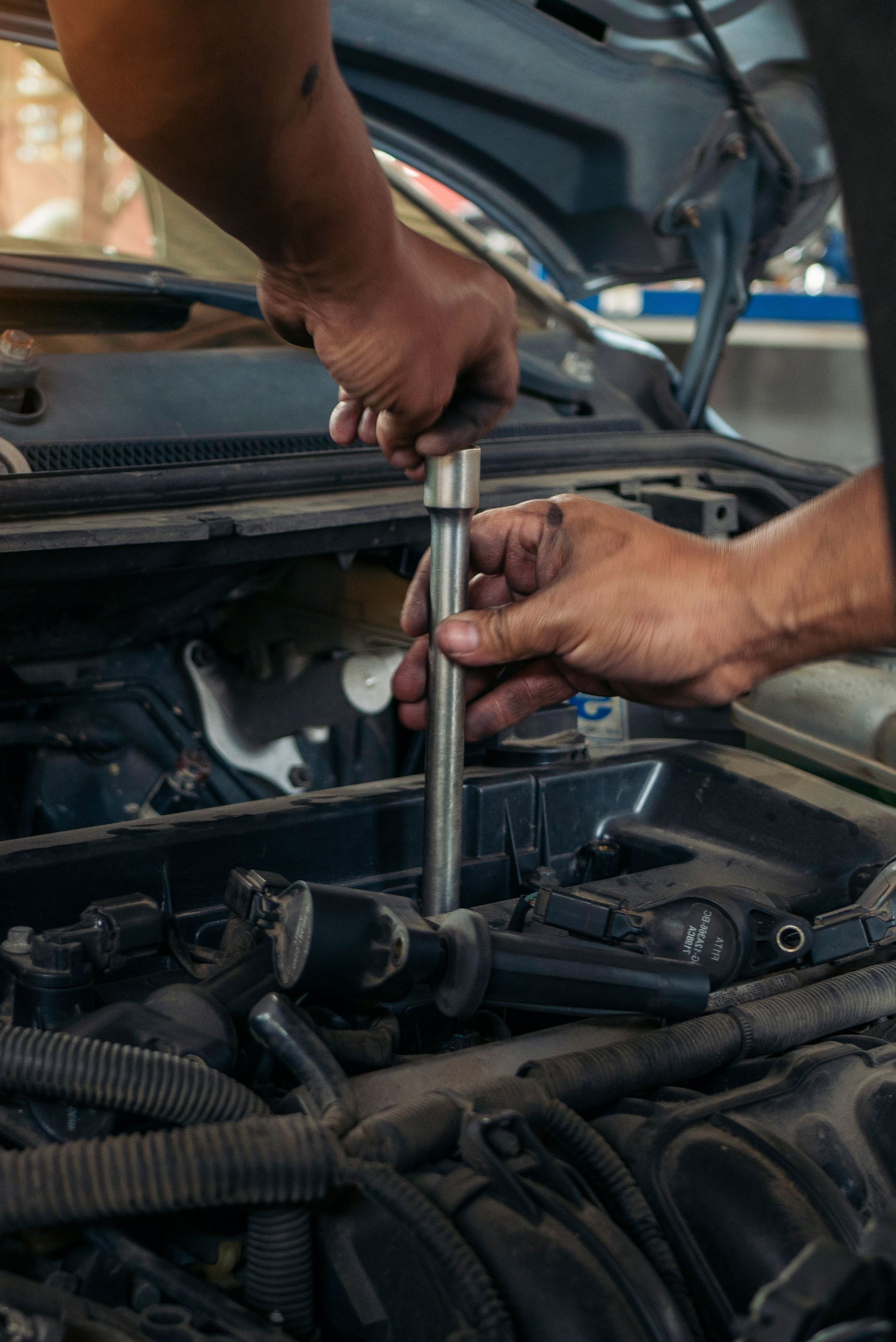 Hands of a mechanic using a tool on a car engine under the hood.