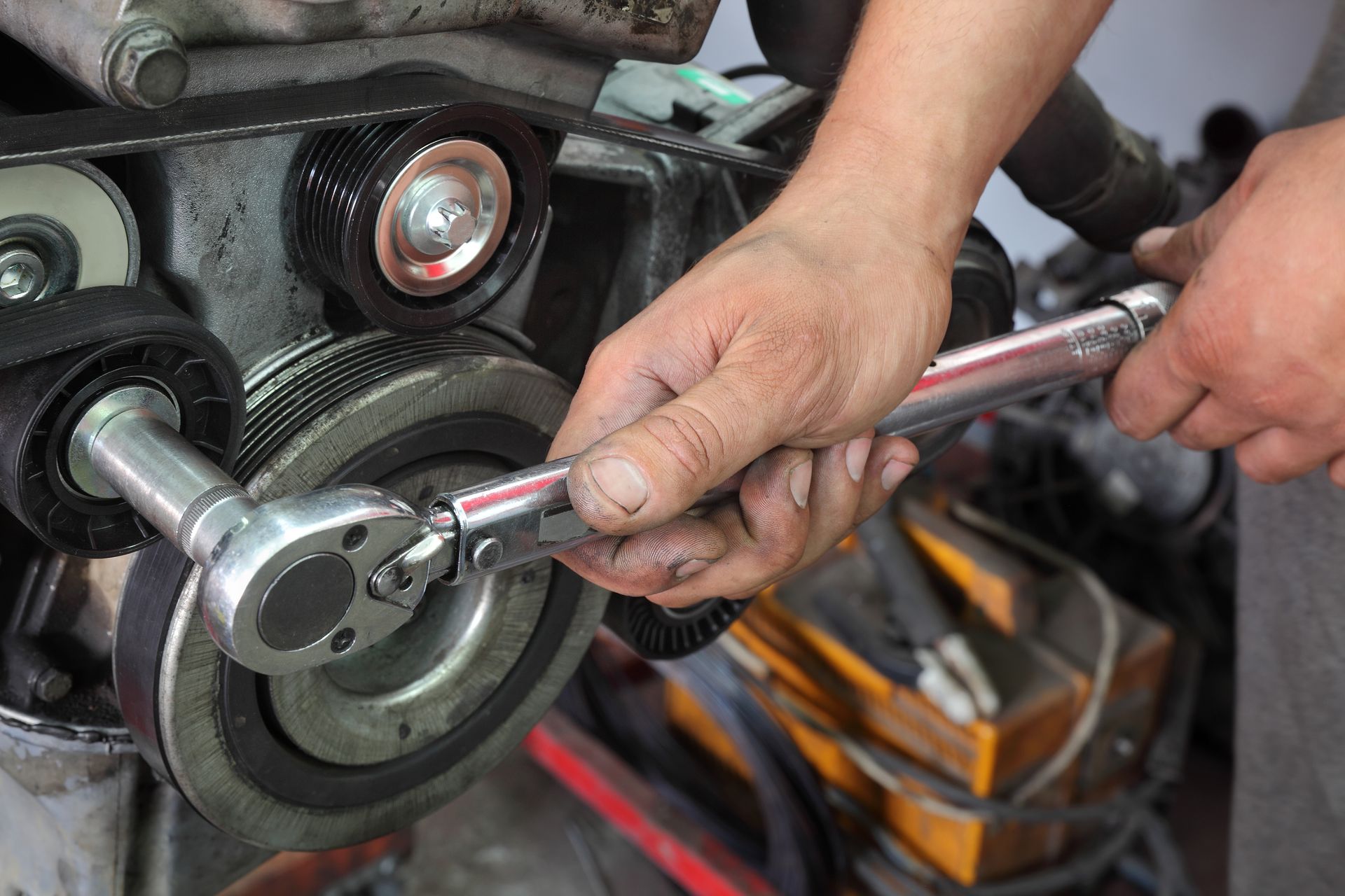 Mechanic using a torque wrench on a car engine pulley, in a garage setting. Mechanic using a torque wrench on a car engine pulley, in a garage setting.