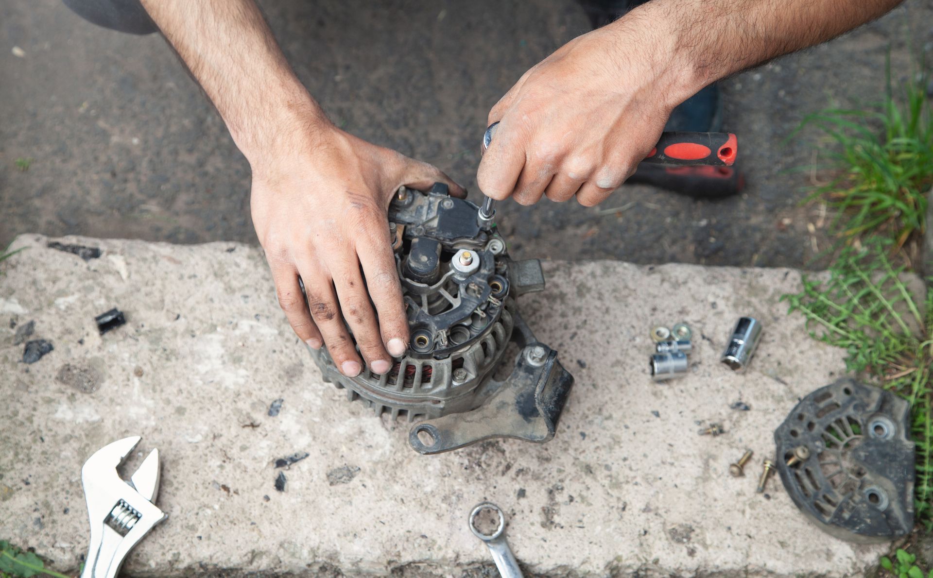 Person repairs car alternator with tools on concrete. Person repairs car alternator with tools on concrete.