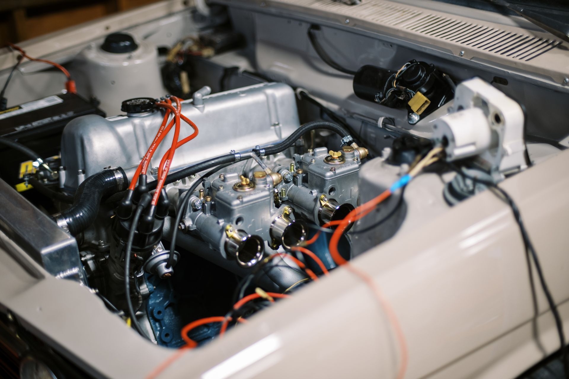 Engine of a vintage car with dual carburetors, red spark plug wires, and electrical wiring. Engine of a vintage car with dual carburetors, red spark plug wires, and electrical wiring.