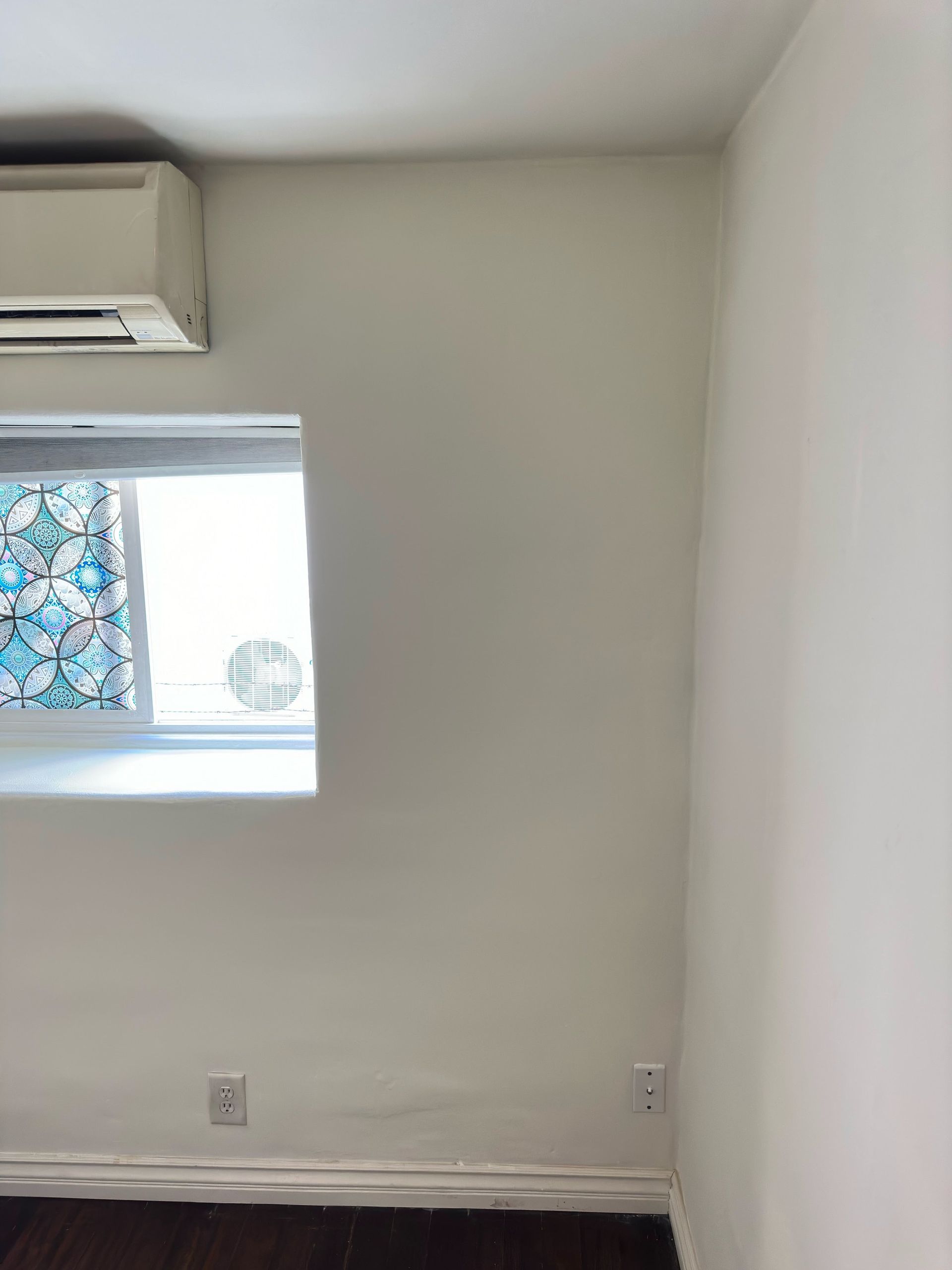 A room with a window , air conditioner , and stained glass window.