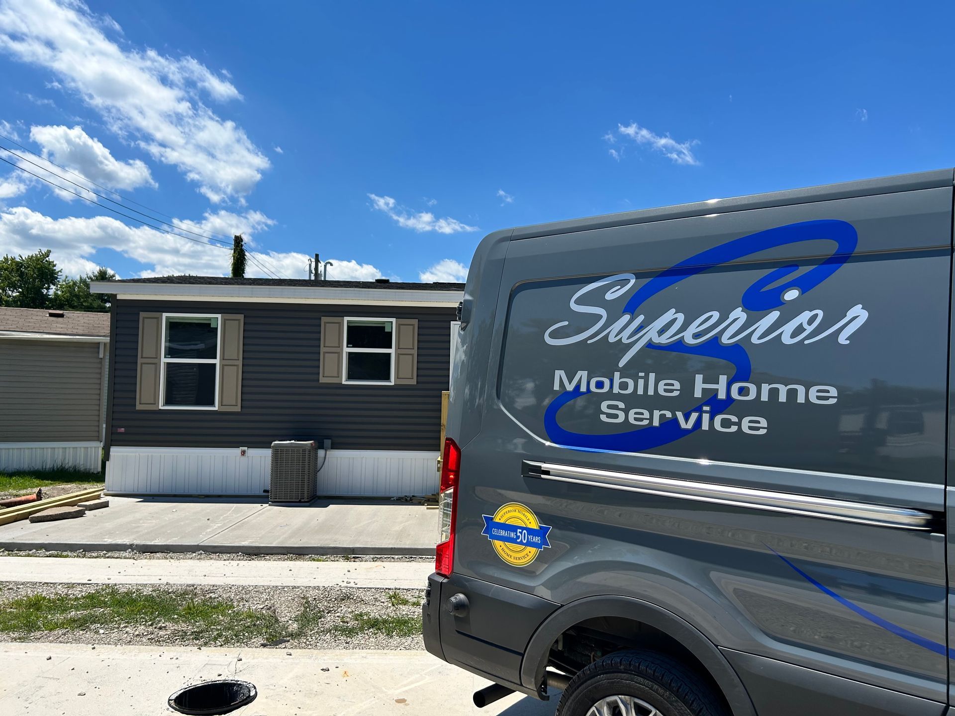 Black service van labeled “Superior Mobile Home Services” parked beside a gray house under a blue sky.