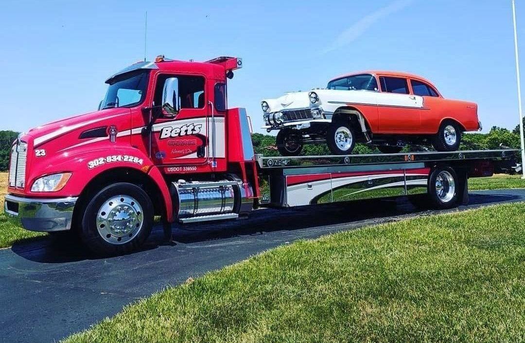 Betts Garage tow truck transporting a classic orange car for service