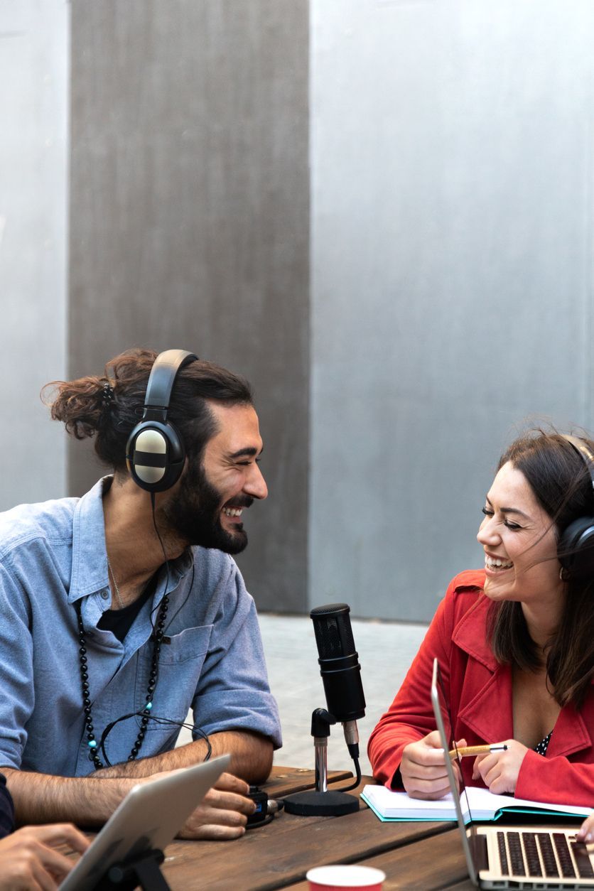 A man and a woman are sitting at a table wearing headphones.
