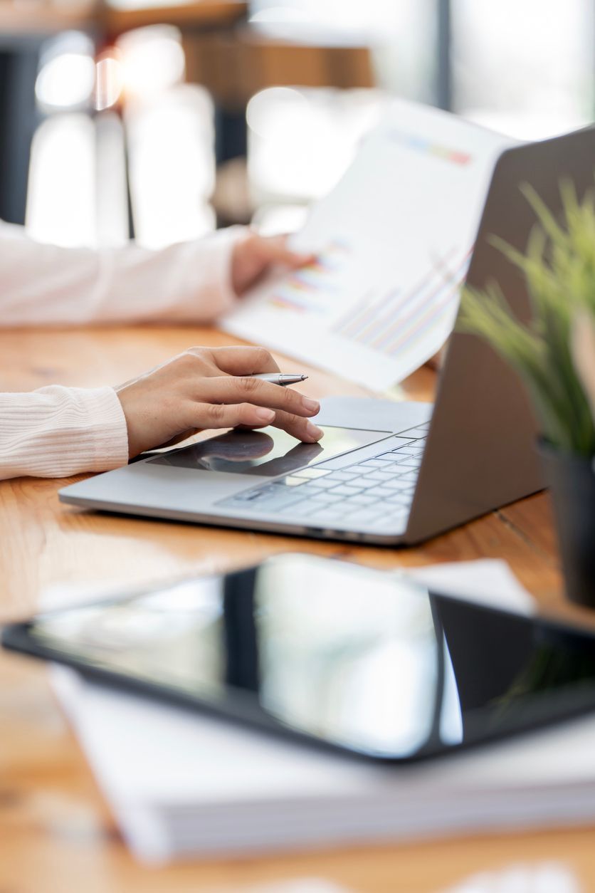 A person is typing on a laptop computer while holding a piece of paper.