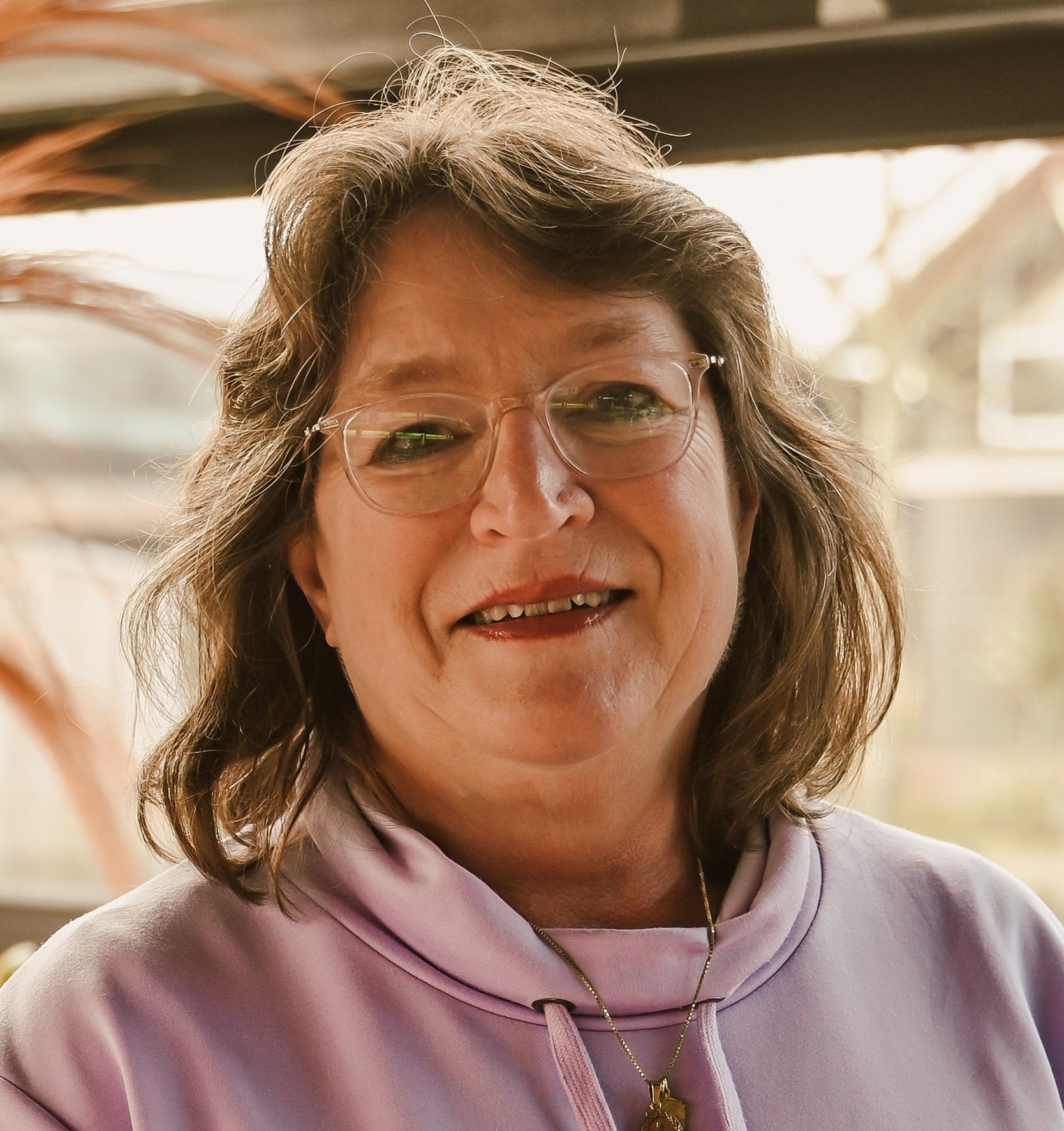 Een vrouw met een bril en een paarse trui lacht naar de camera