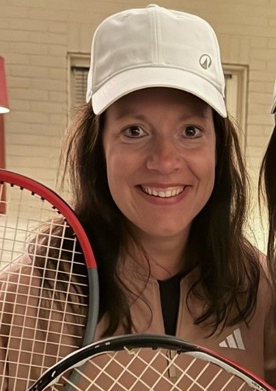 Een lachende vrouw met een tennisracket in haar hand en een witte pet op.