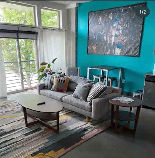 Living room with gray sofa, teal accent wall, and large art print. Rug has pink and yellow stripes.