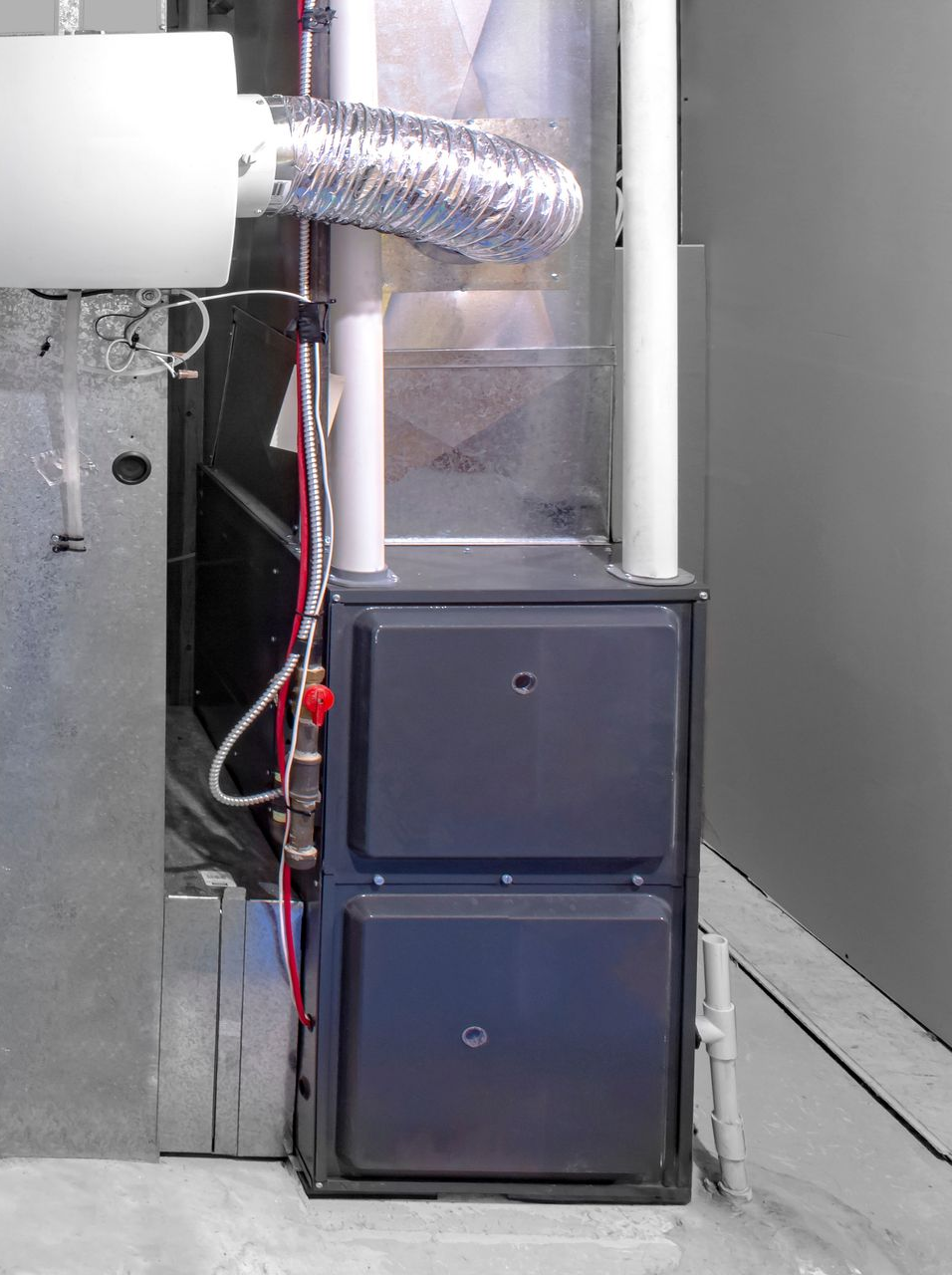 Fournaise grise à deux portes, entourée de conduits métalliques, à côté d'un mur.