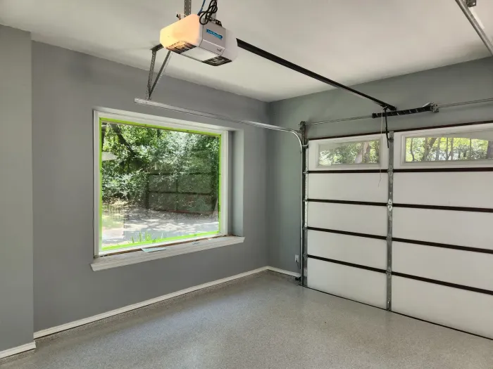 An empty garage with a garage door open and a window.