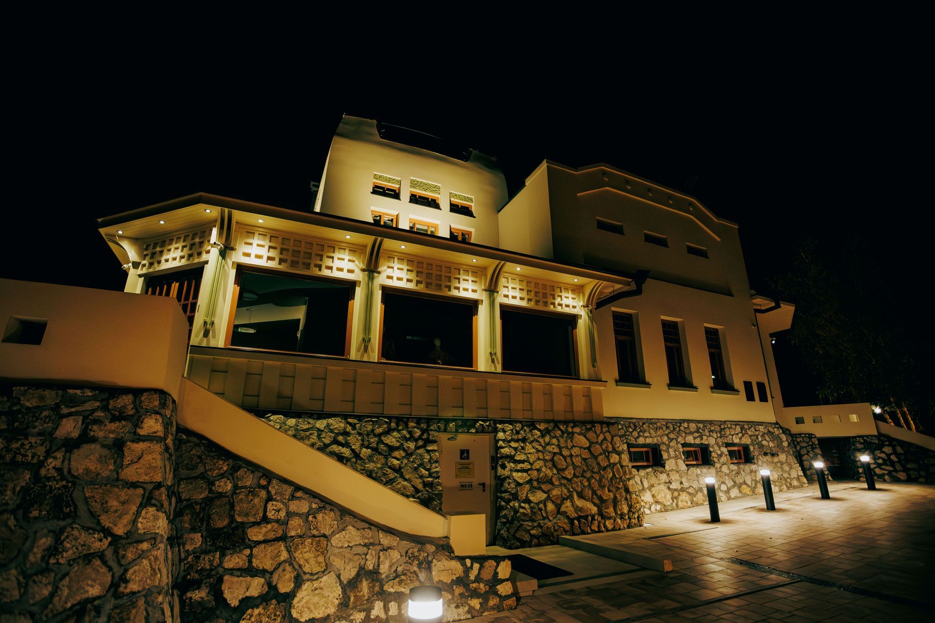 Illuminated stone building at night with a terrace and warm yellow lights