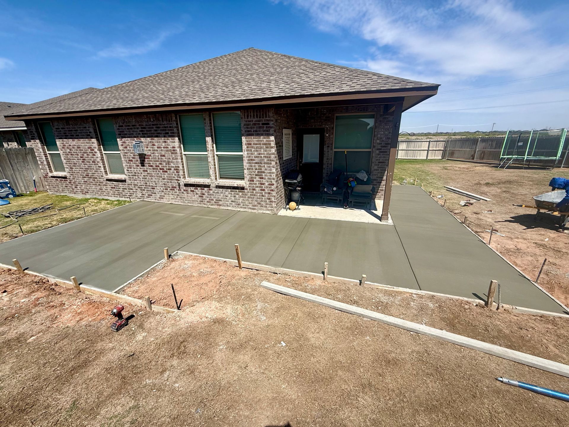 New concrete patio under construction beside a stone house in a suburban yard