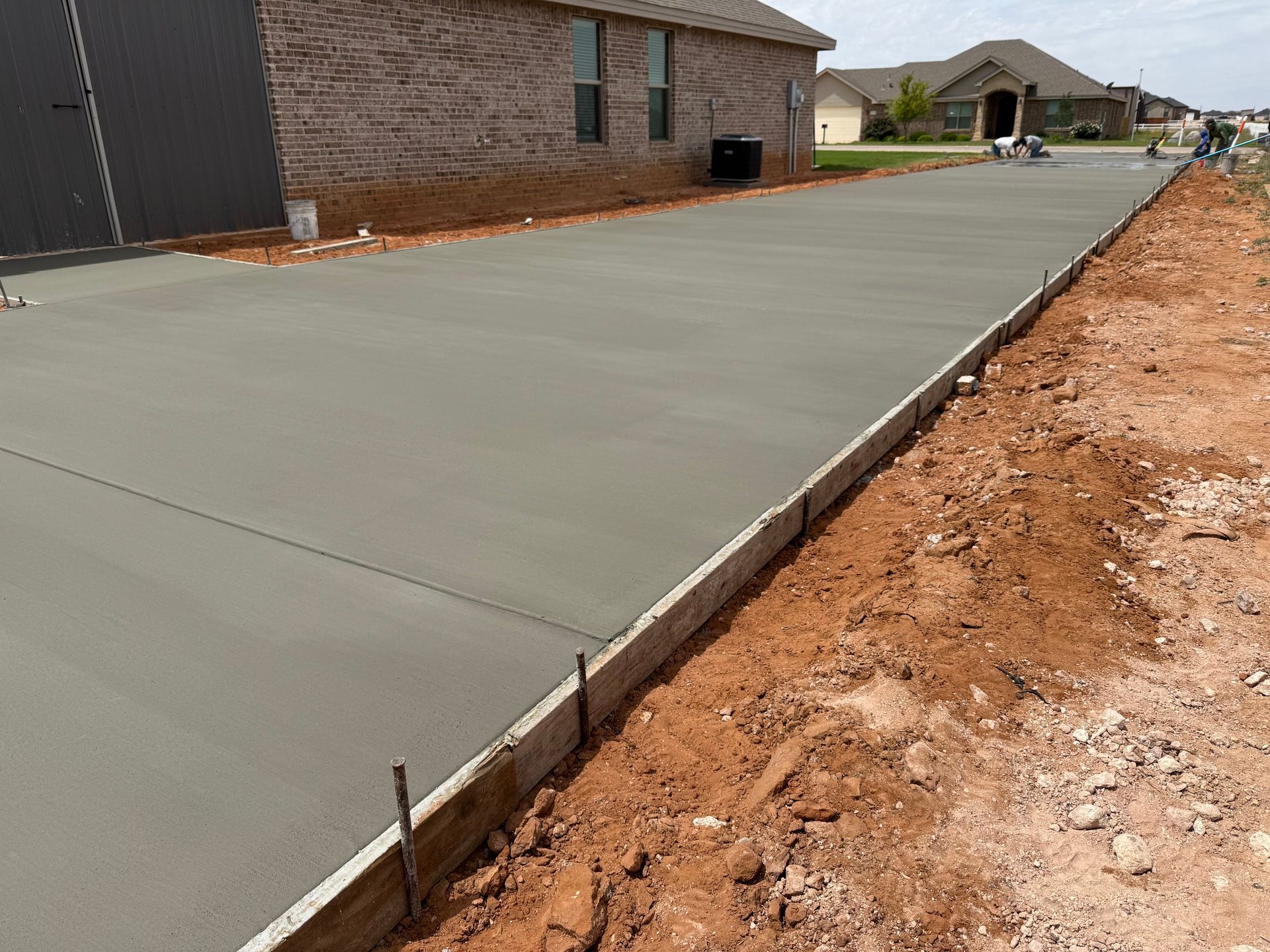 Freshly poured concrete driveway beside a brick house under construction, with dirt along the edges