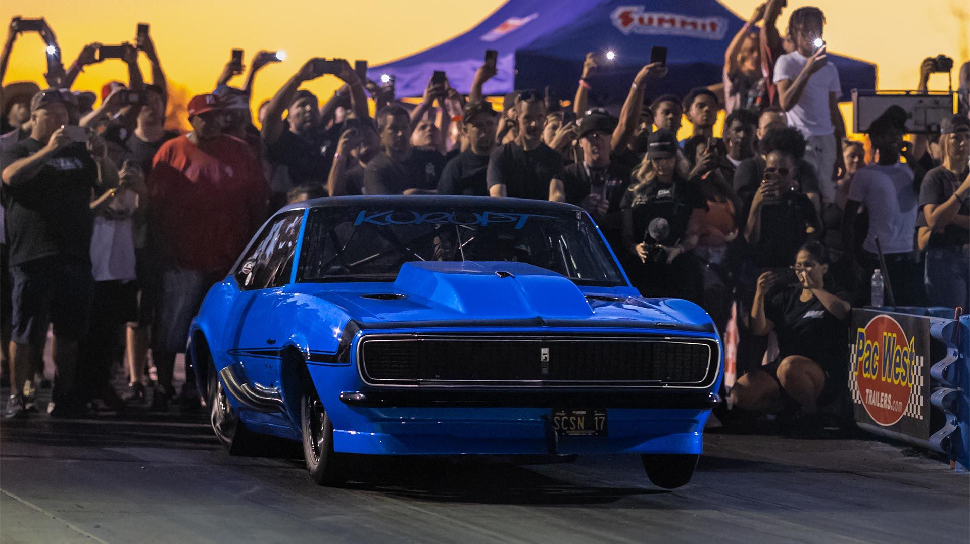 Blue race car on track, crowd cheering, sunset background.
