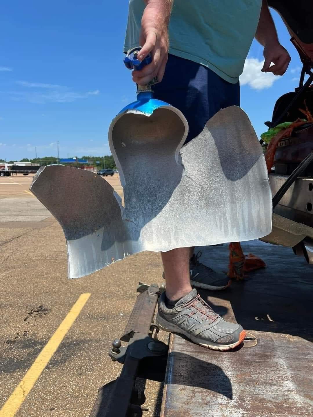 Person holding a large, torn metal object, likely part of an industrial component, outdoors.