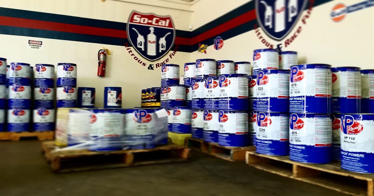 Warehouse storage of blue and white oil drums on wooden pallets, with a So-Cal logo on the wall.