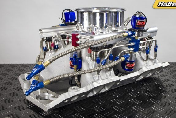 Silver and blue Haltech fuel injection manifold on a checkered surface.
