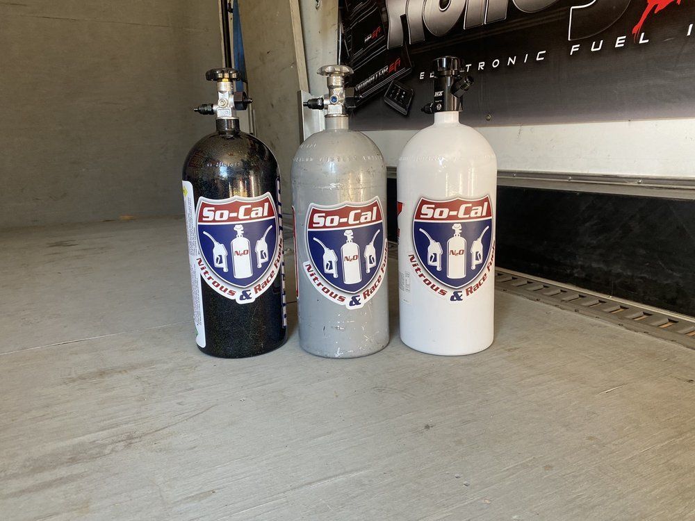 Three nitrous oxide bottles in black, grey and white with So-Cal labels, standing on concrete.