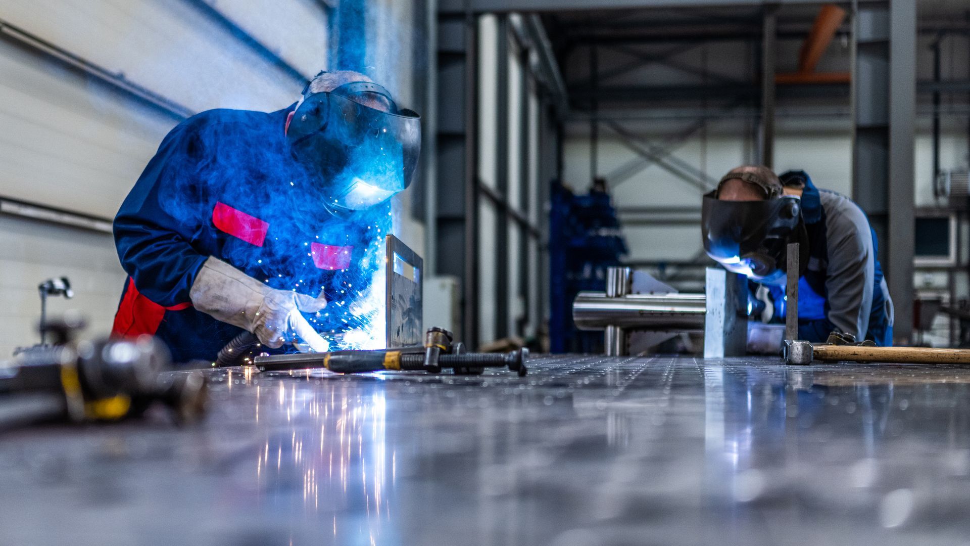 A man is welding a metal pipe in a factory.