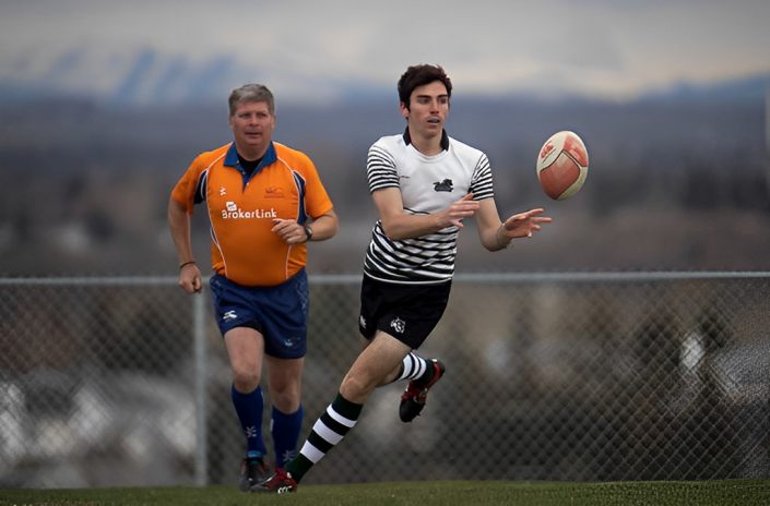 A rugby player in a striped jersey reaches for a ball in mid-air, with a referee in an orange shirt running behind him.
