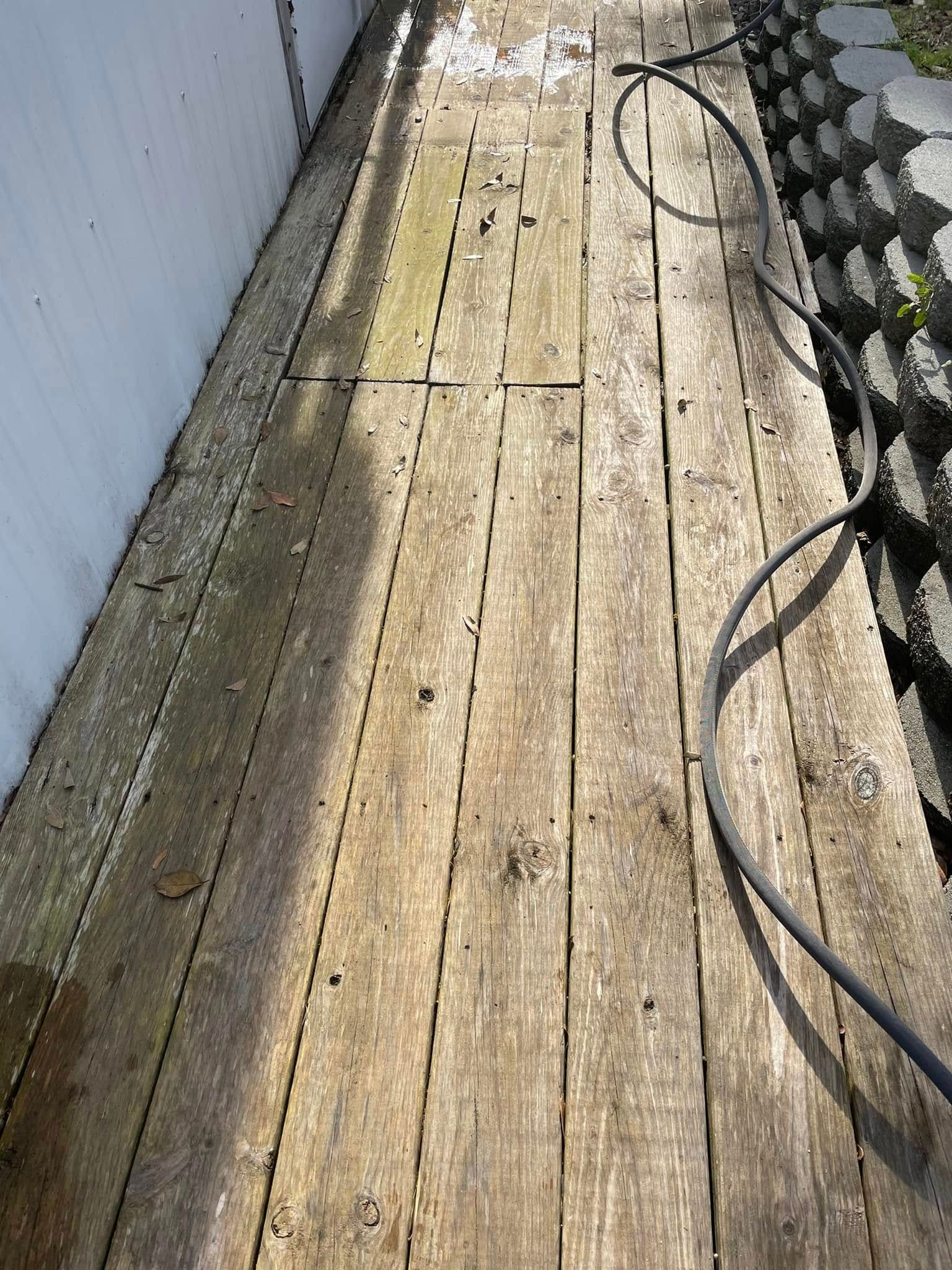 Weathered wooden walkway beside a white wall, with coiled black hoses on the right.