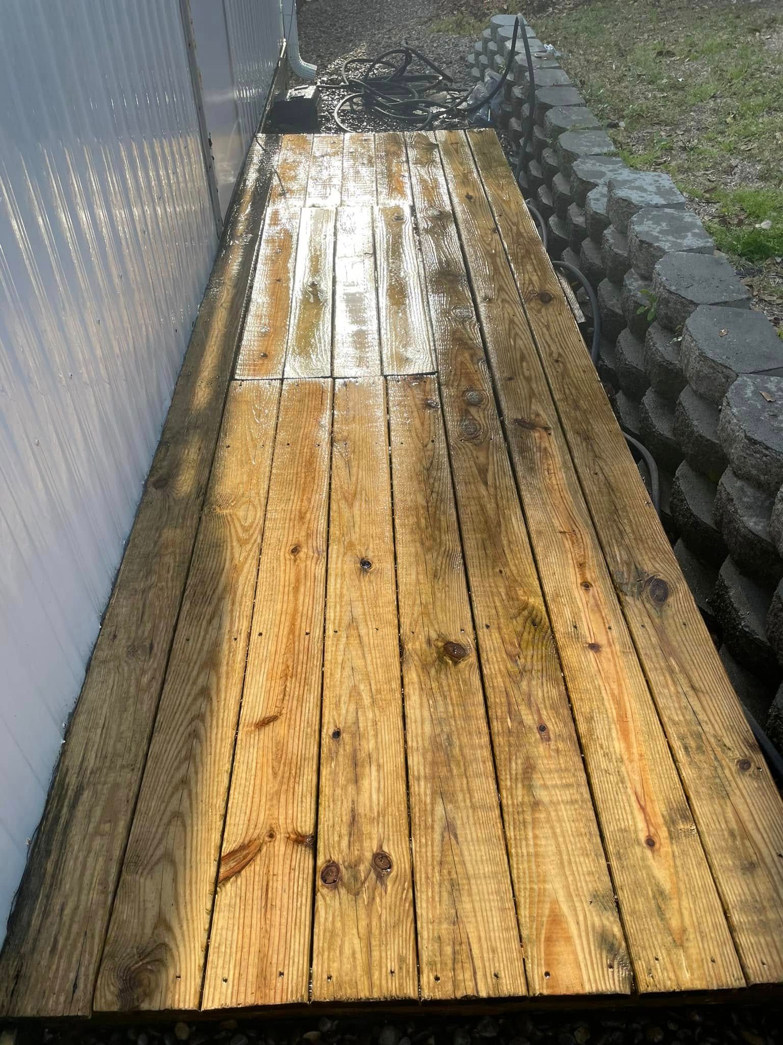 Wet wooden walkway beside a chain-link fence and stone border, with puddles reflecting light.