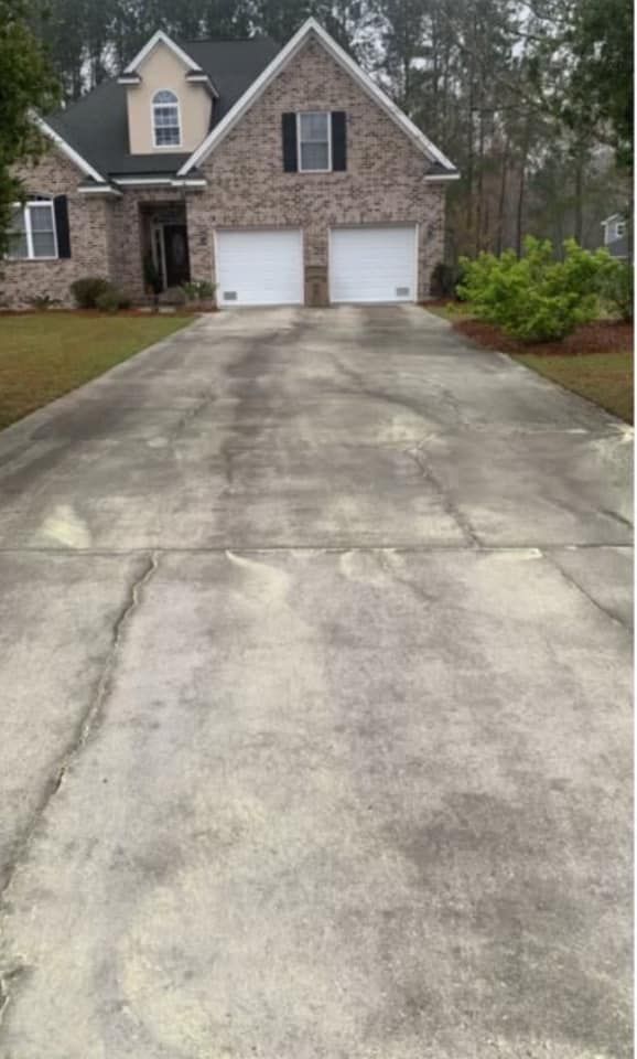 Brick house with double garage and a long concrete driveway, surrounded by trees and shrubs