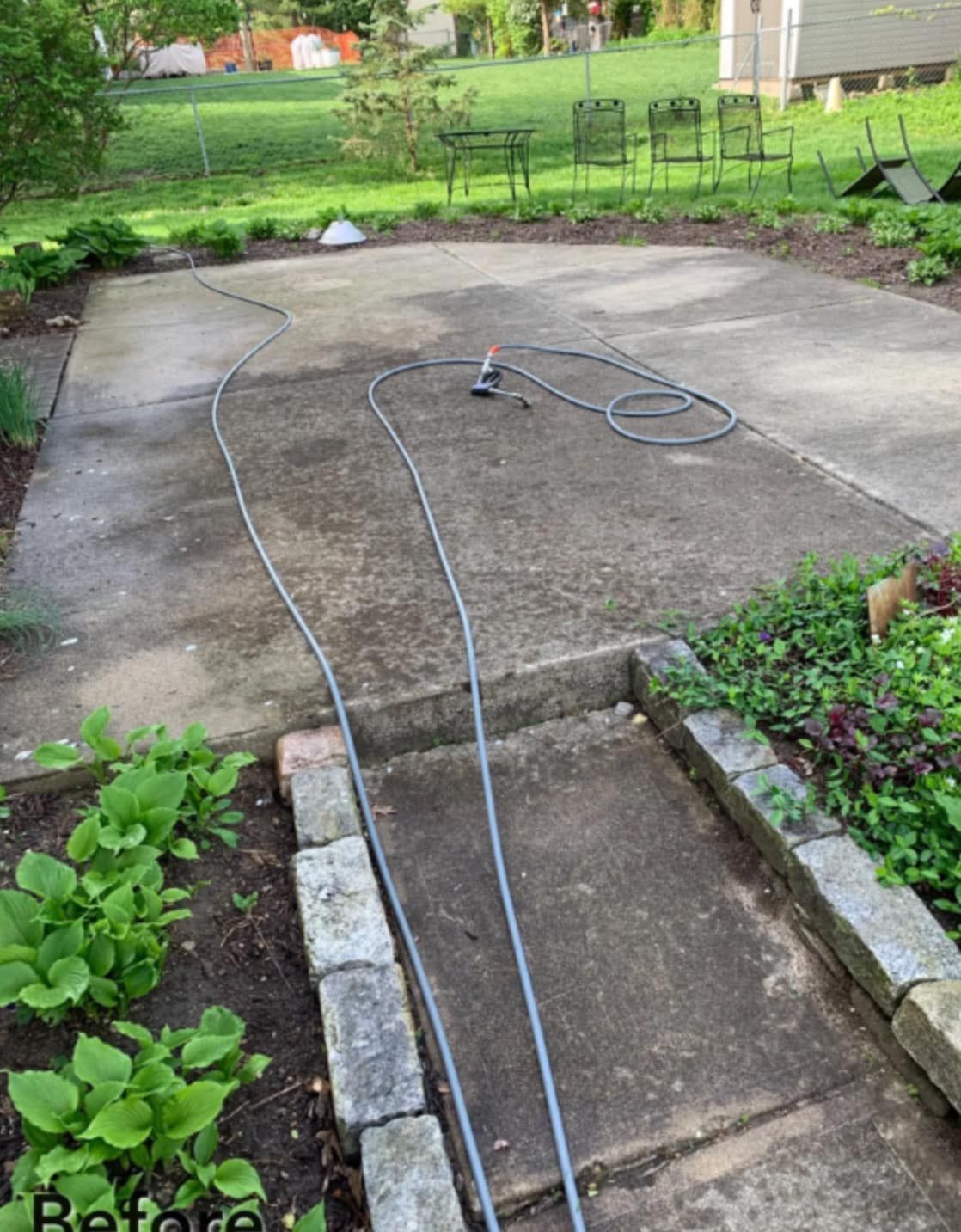 Concrete patio with two long black hoses or cables lying across it in a backyard garden.