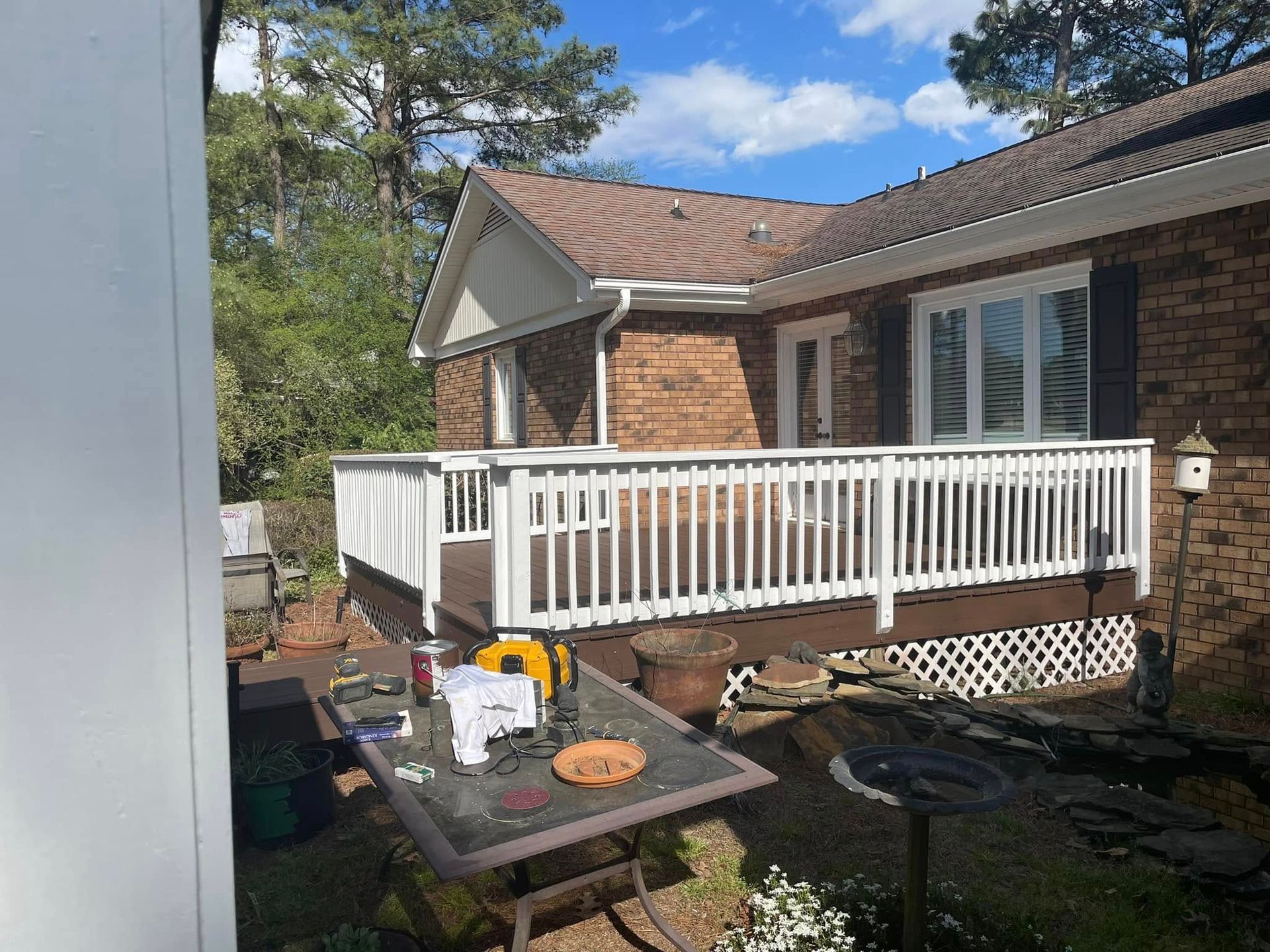 Brick house with white deck railing and outdoor table in a sunny backyard.