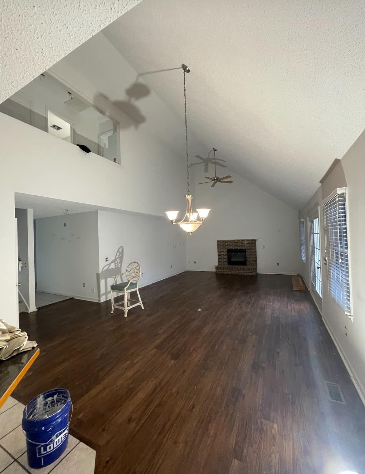 Spacious empty living room with hardwood floors, fireplace, chandelier, and large windows with blinds