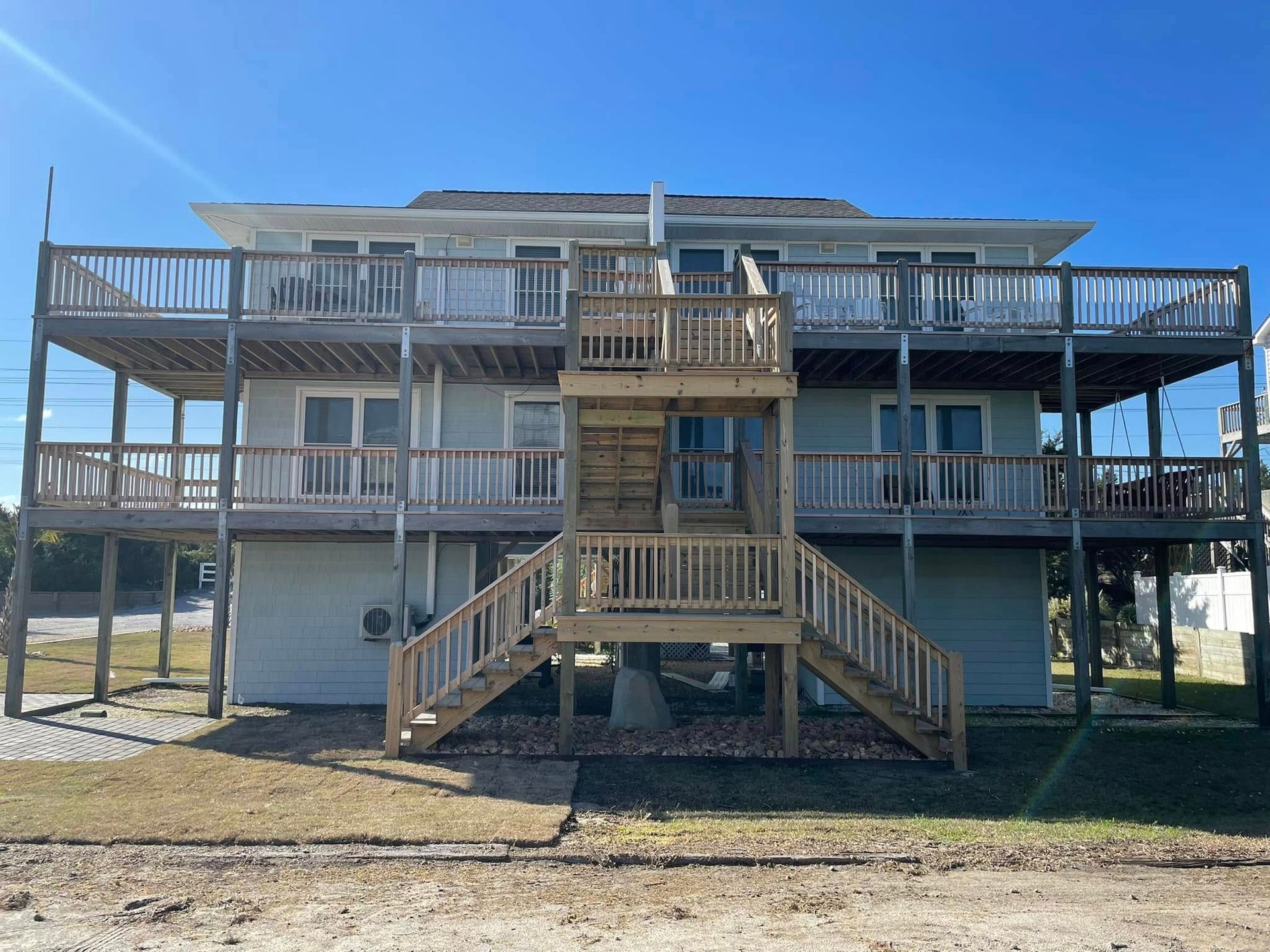 Two-story elevated beach house with wide wraparound porches and central stairs under a clear blue sky