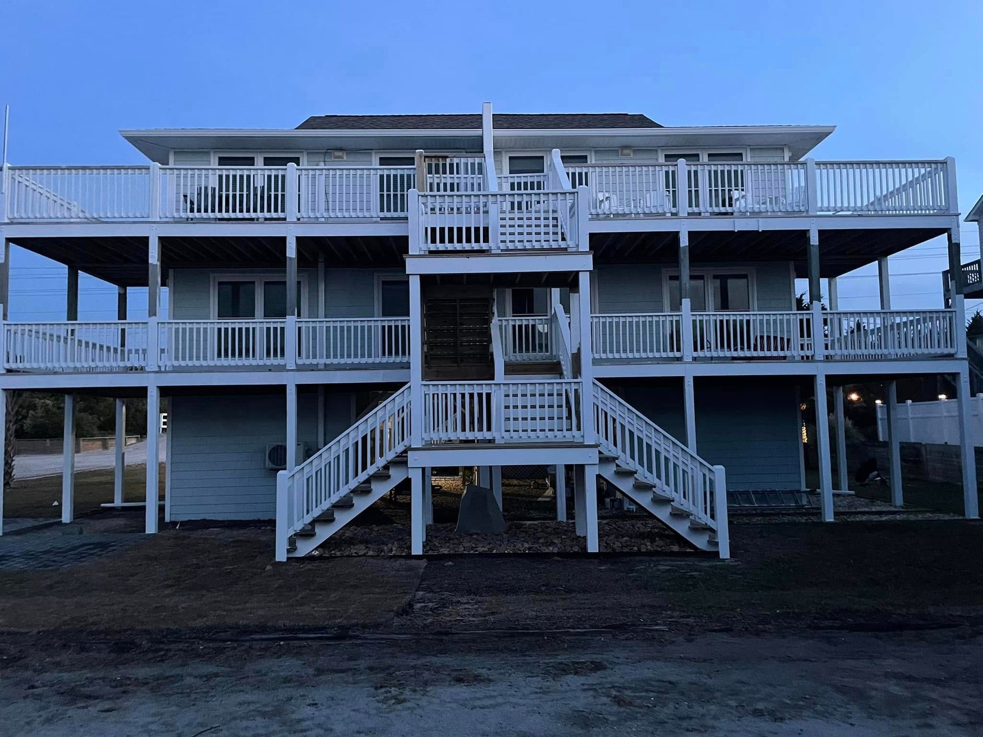 White beach house with wraparound porches and central stairs in dim evening light