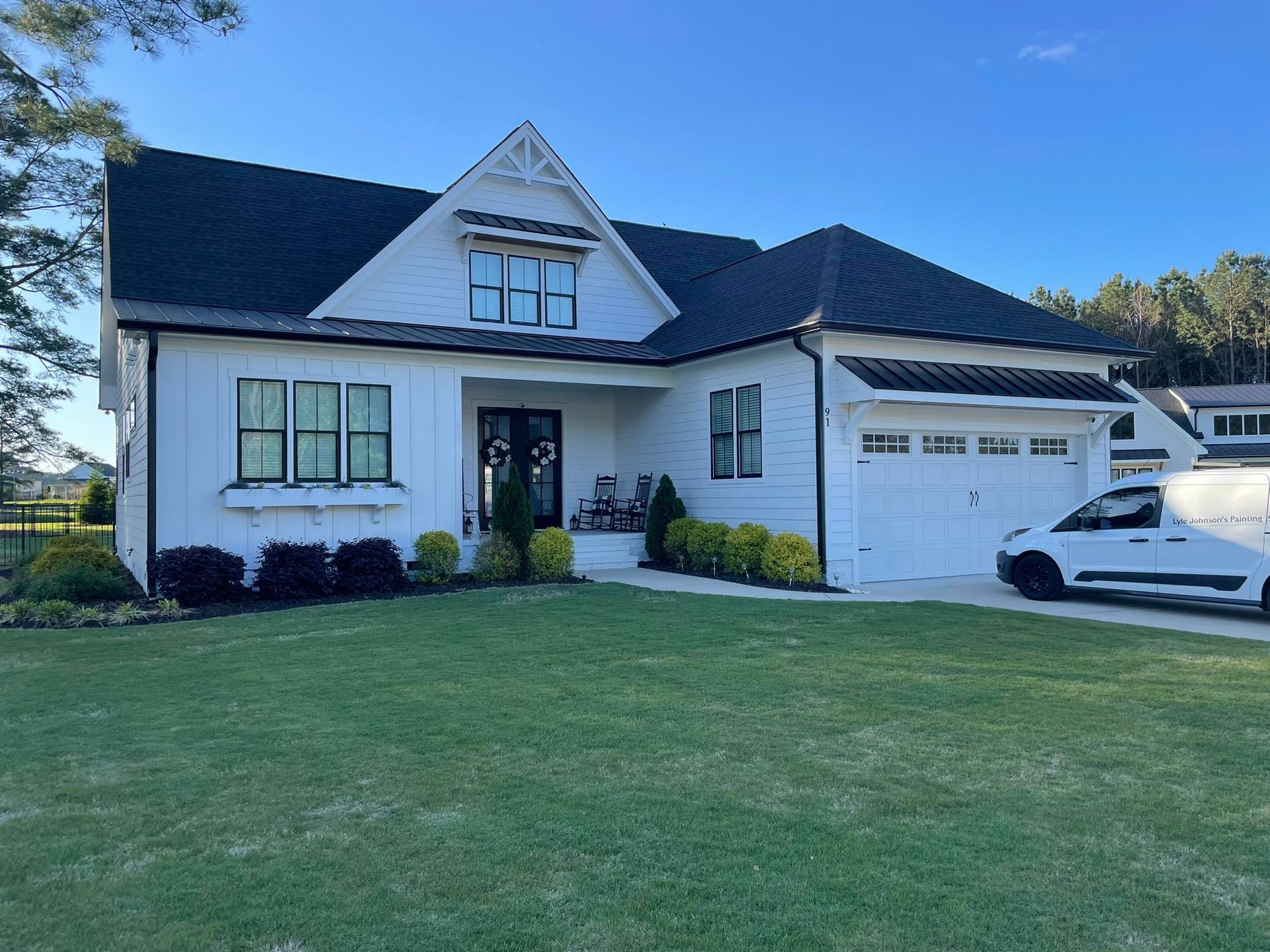 White suburban house with dark roof, front lawn, and garage under a clear blue sky