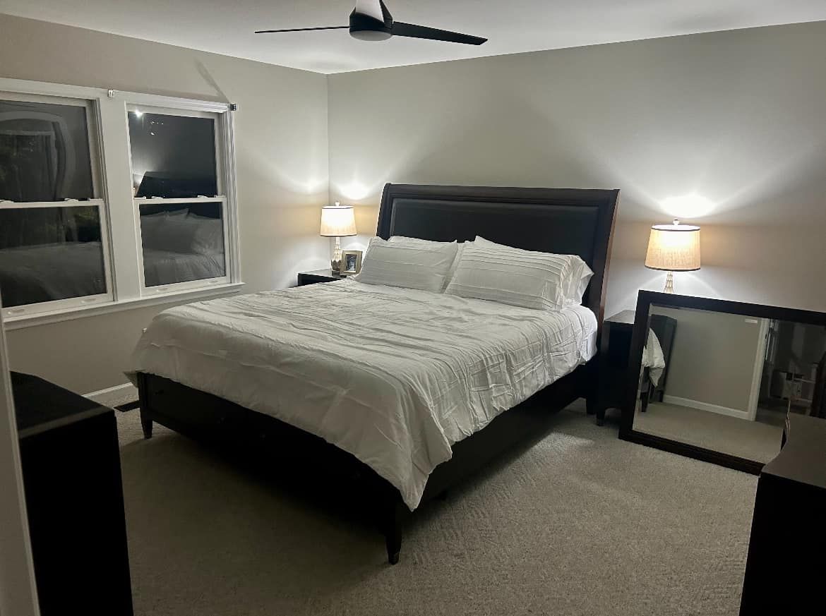 Bedroom with a neatly made bed, two bedside lamps, ceiling fan, and mirrored nightstands.