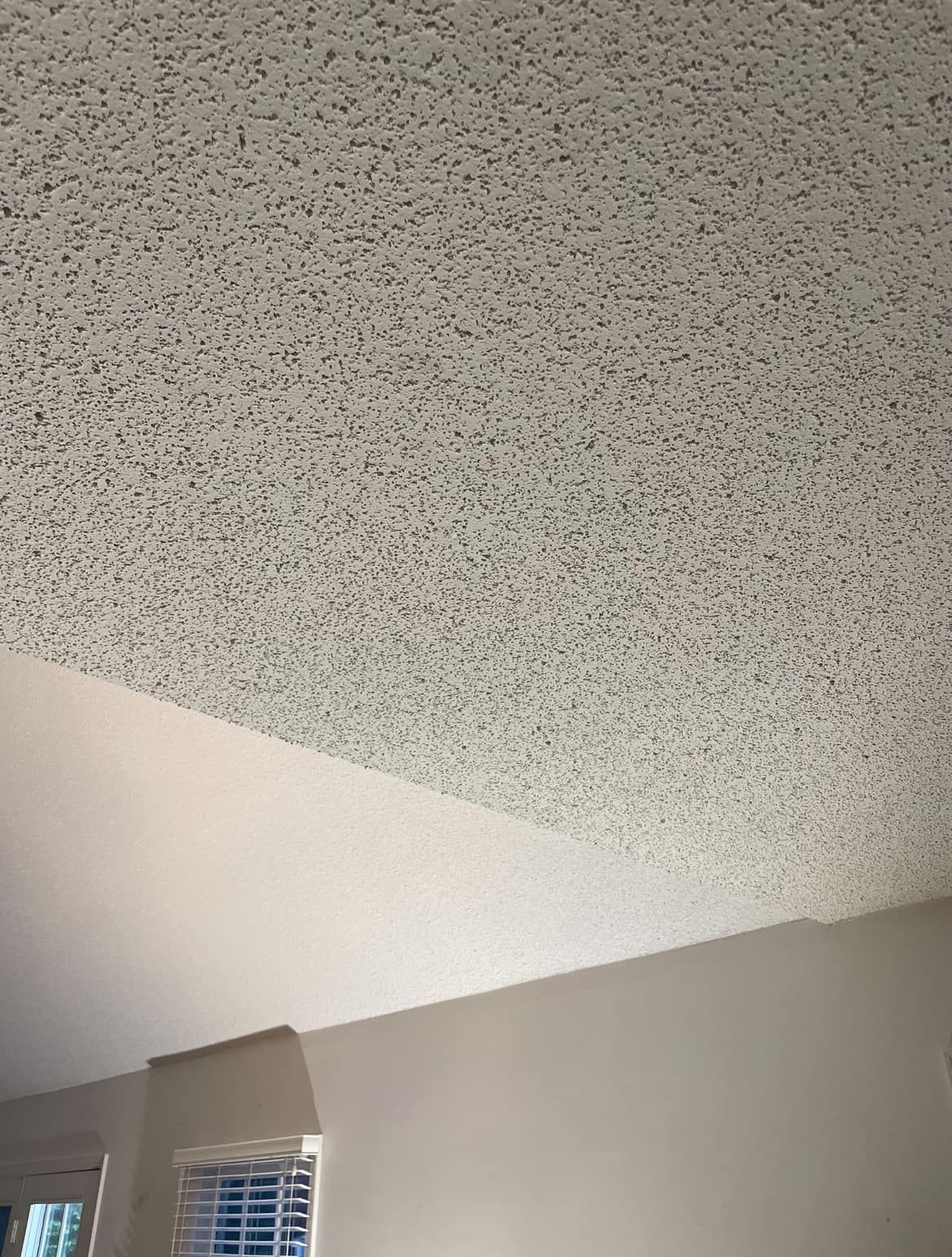 White textured ceiling above a beige wall and small window in a room