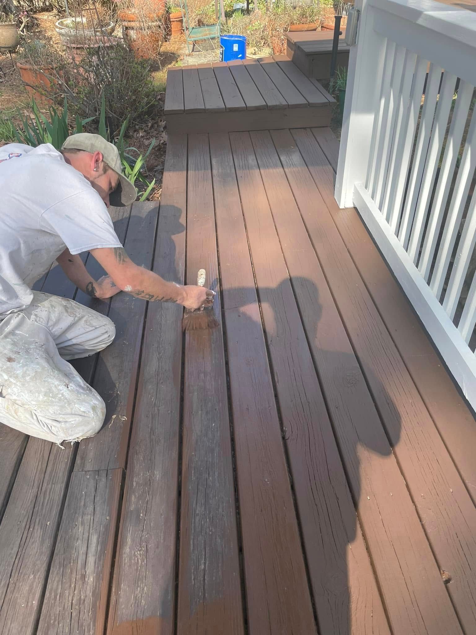 Person painting a brown wooden deck railing and floor with a paintbrush outdoors